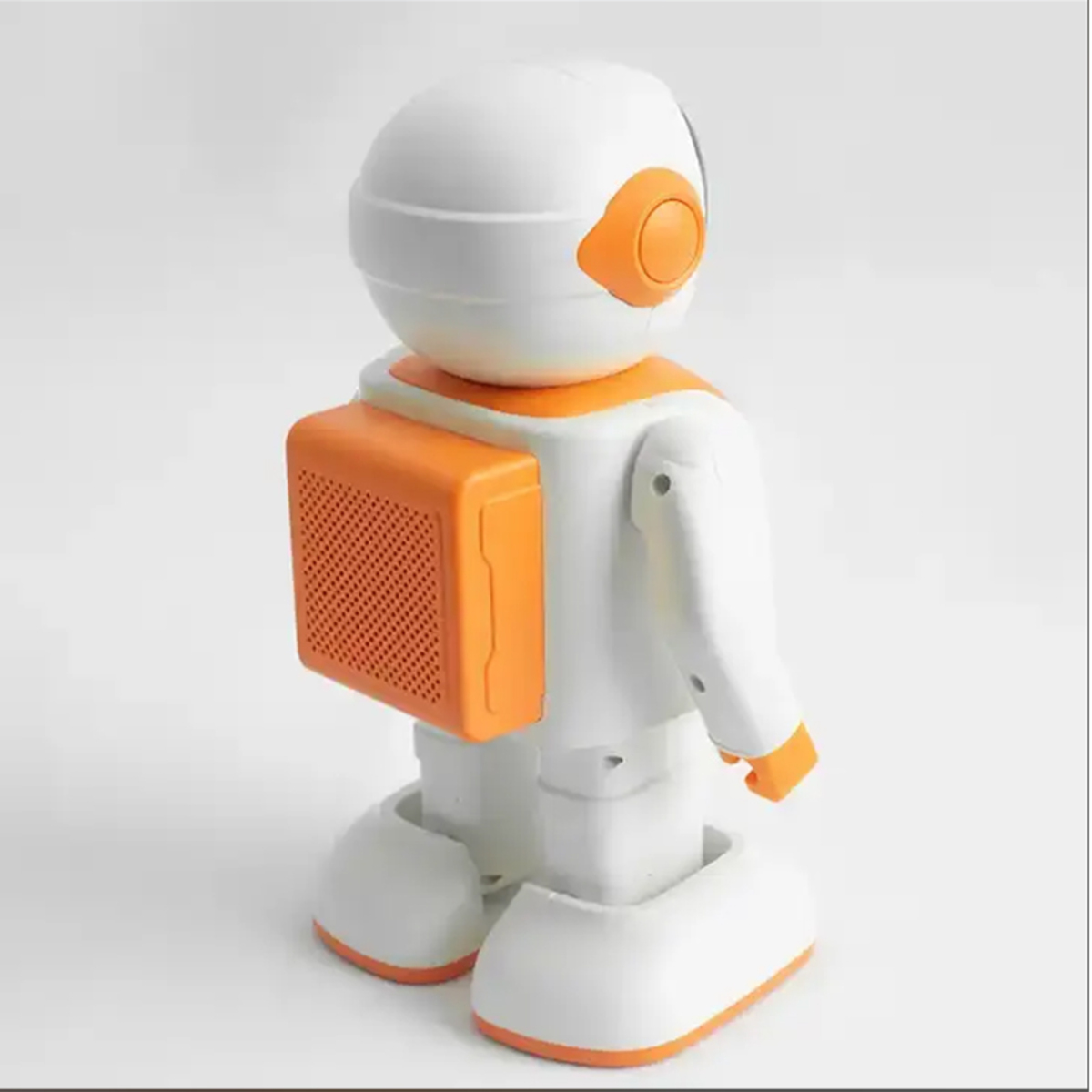 Un juguete de robot blanco y naranja se muestra desde atrás. Tiene una cabeza redonda, un altavoz naranja y detalles en naranja en brazos y pies.