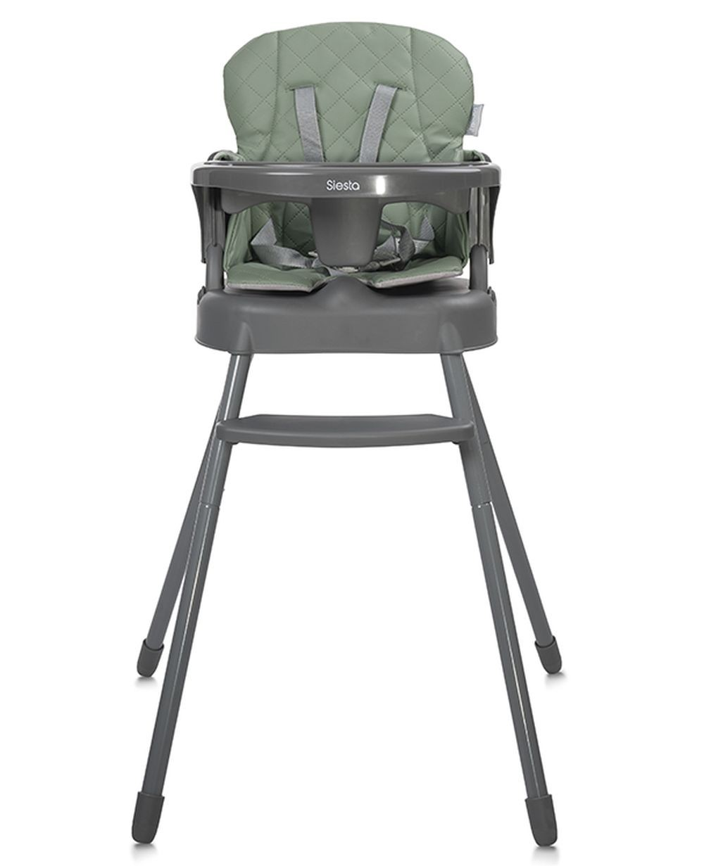 Una trona para bebé con asiento verde, estructura gris y correas de seguridad, con la etiqueta 'Siesta'. Está sobre fondo blanco.
