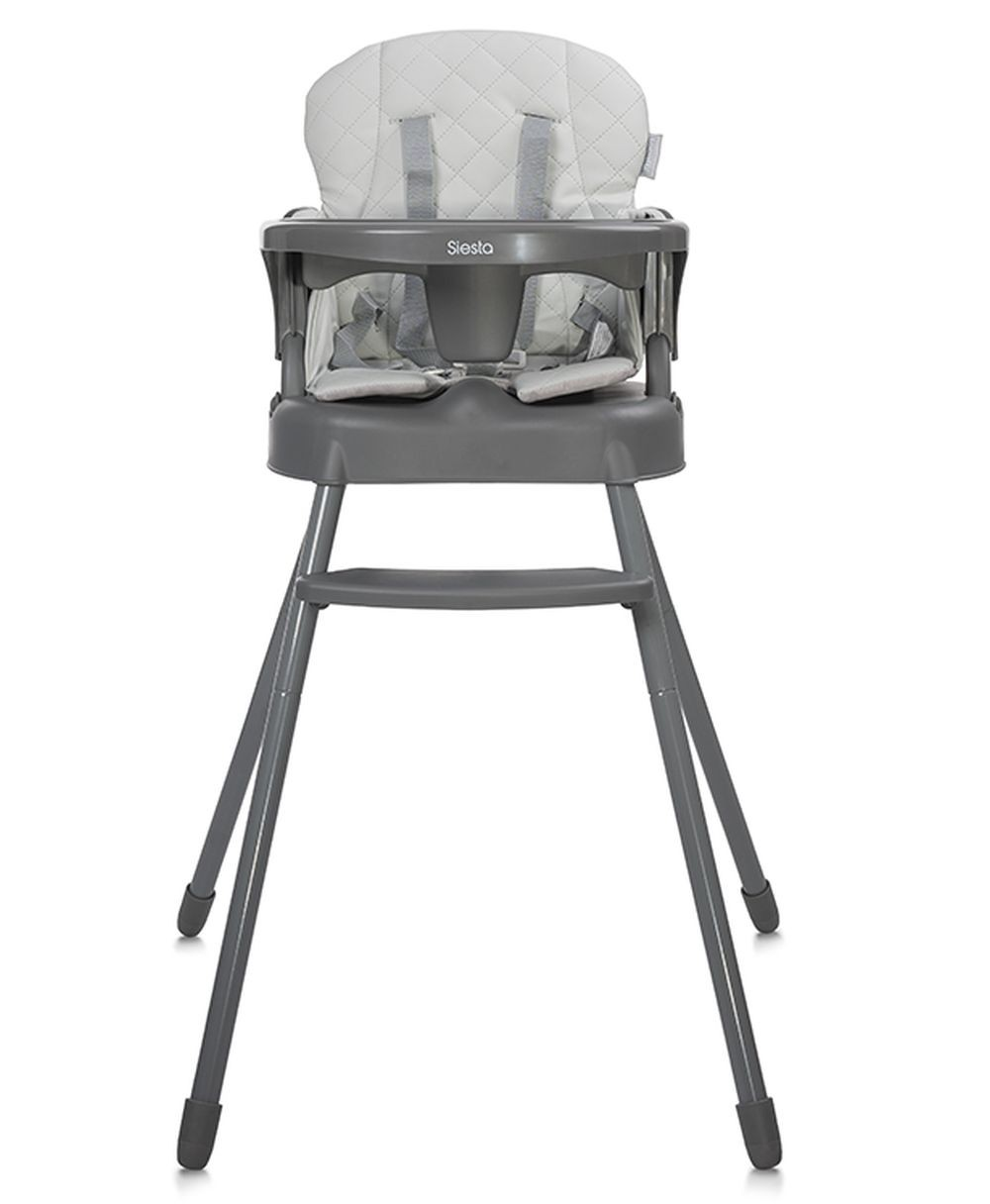 Una trona gris con asiento acolchado blanco y correas. La silla tiene una bandeja y patas. La palabra "Siesta" es visible.