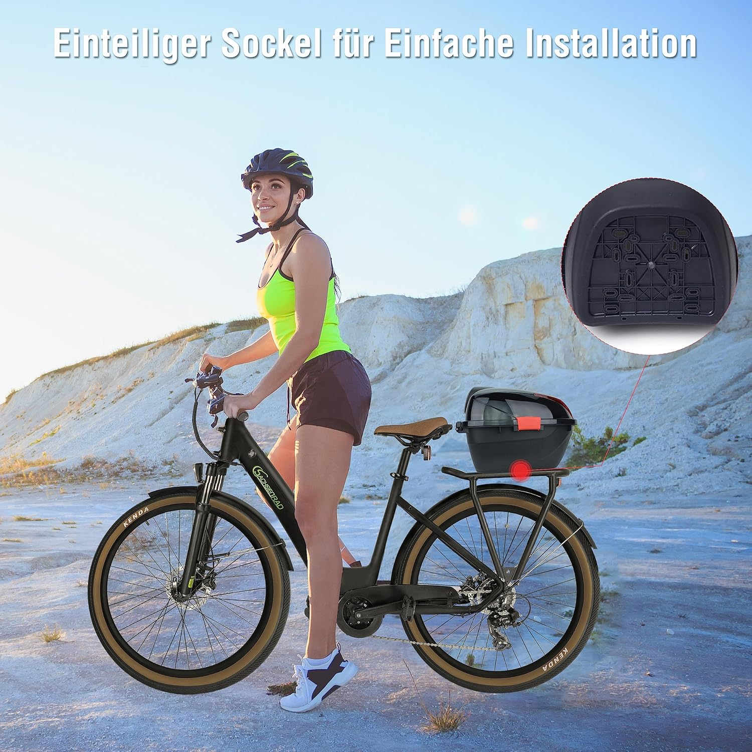 Eine Frau mit Helm fährt ein schwarzes Fahrrad mit einer Aufbewahrungsbox. Der Hintergrund zeigt eine Landschaft mit klarem Himmel und Berg.
