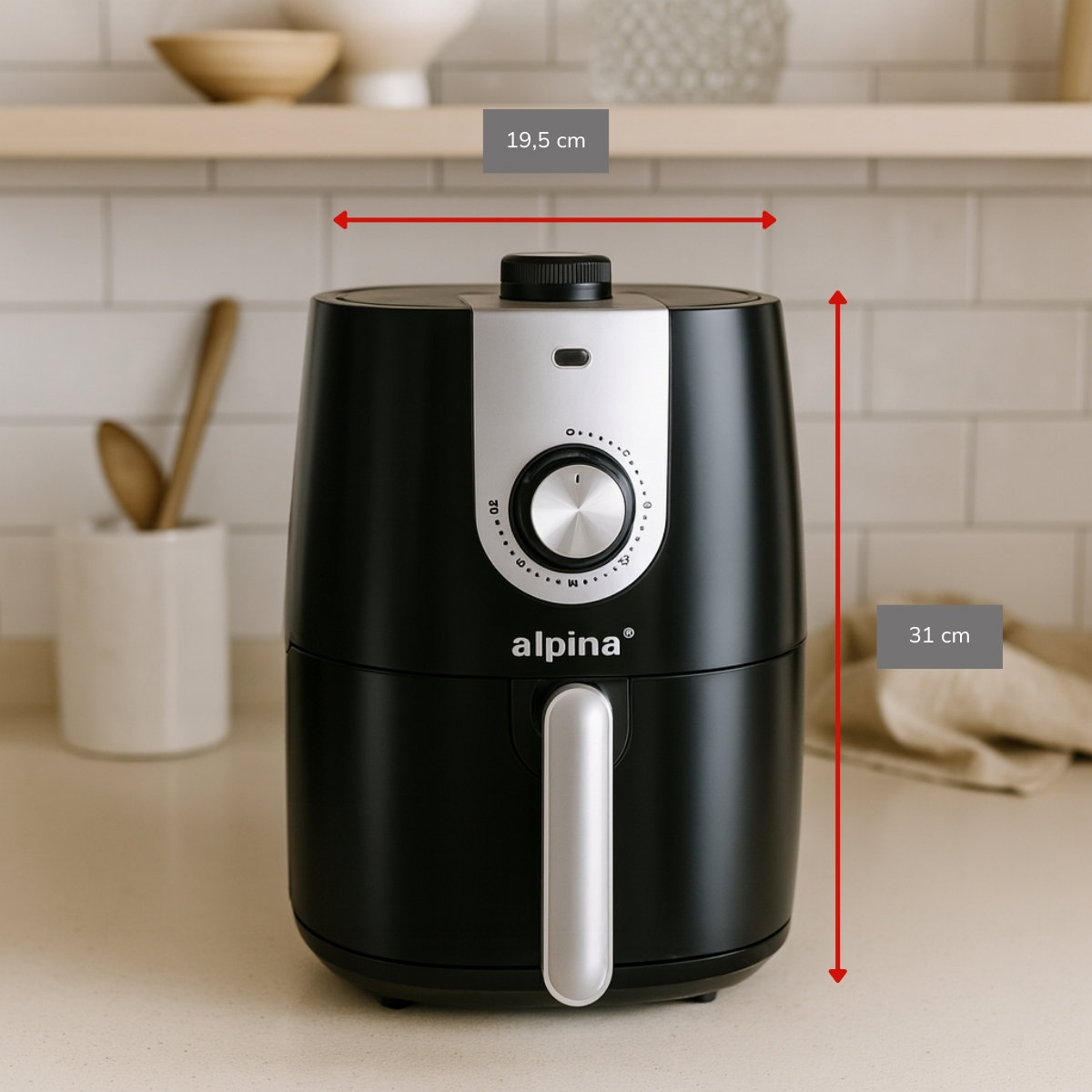 Zwarte airfryer met zilveren accenten. De afbeelding toont afmetingen. Achtergrond heeft plank, houten lepels en een witte pot.