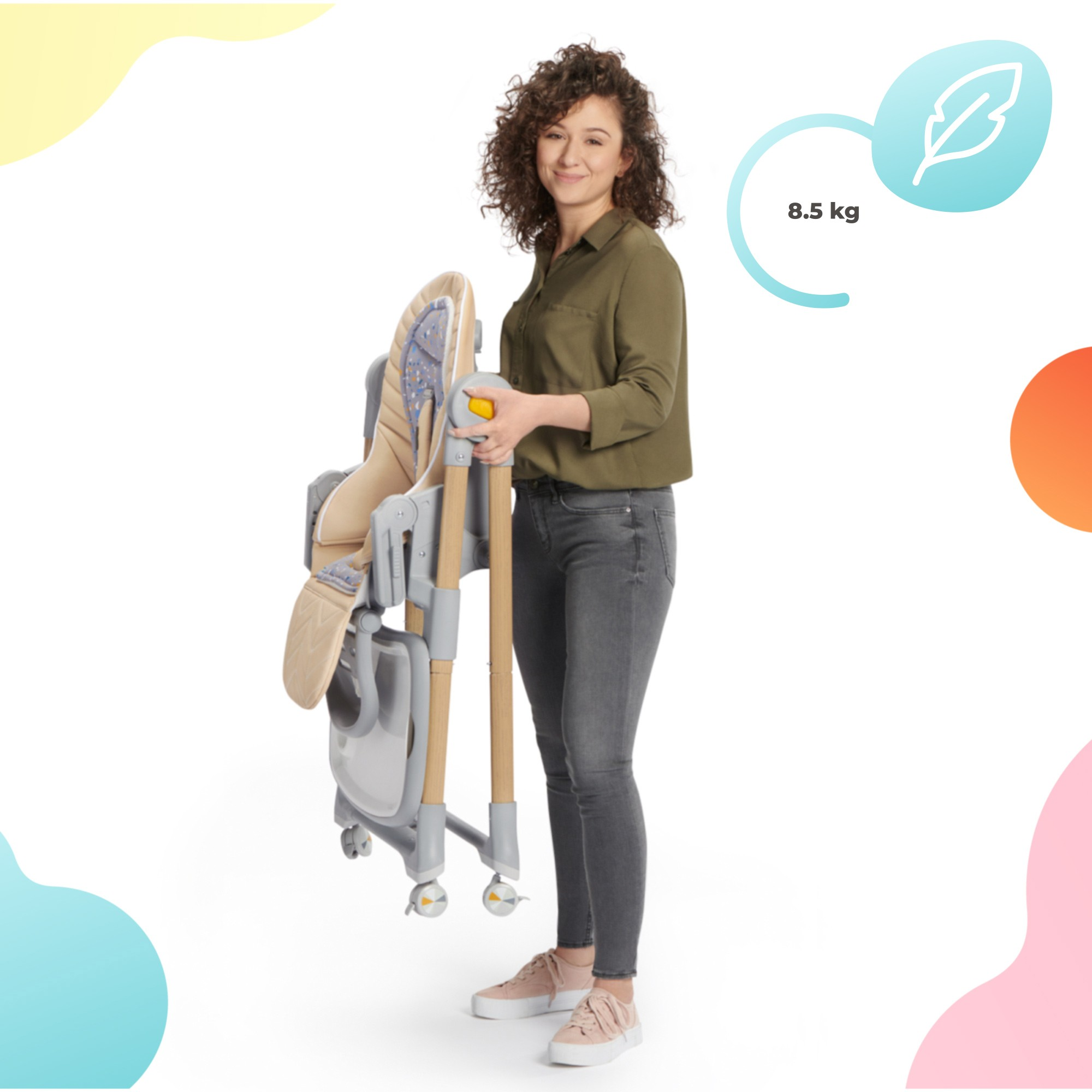 Eine Frau hält einen zusammengeklappten Babyhochstuhl. Er ist grau, beige und aus Holz. Der Stuhl wiegt 8,5 kg. Frau trägt grünes Hemd und graue Hose.