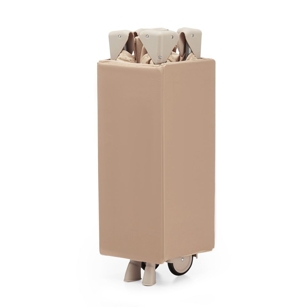 Ein zusammengeklapptes, hellbraunes Babybett mit Rädern. Das Bett ist rechteckig und steht aufrecht. Die Oberseite hat zusammengeklappte beige Stützen.