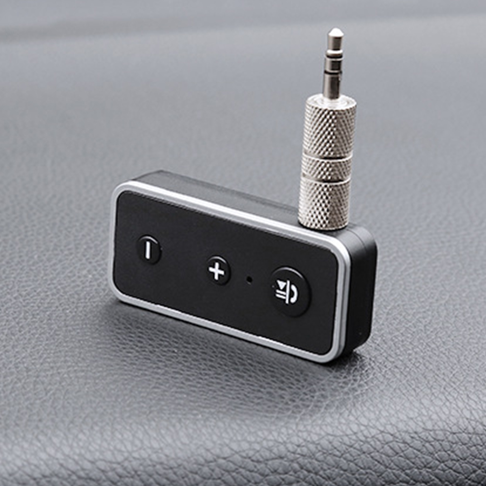Ein schwarzer Audioadapter mit silberner Einfassung und 3,5-mm-Klinke liegt auf einer grauen Oberfläche. Er hat Knöpfe zur Lautstärkeregelung.