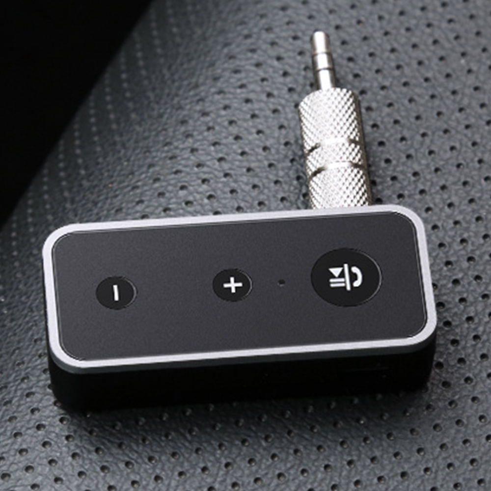 Ein schwarzes Audiogerät mit Knöpfen und einem silbernen Stecker liegt auf einer strukturierten dunklen Oberfläche. Das Gerät hat Lautstärkeregler.