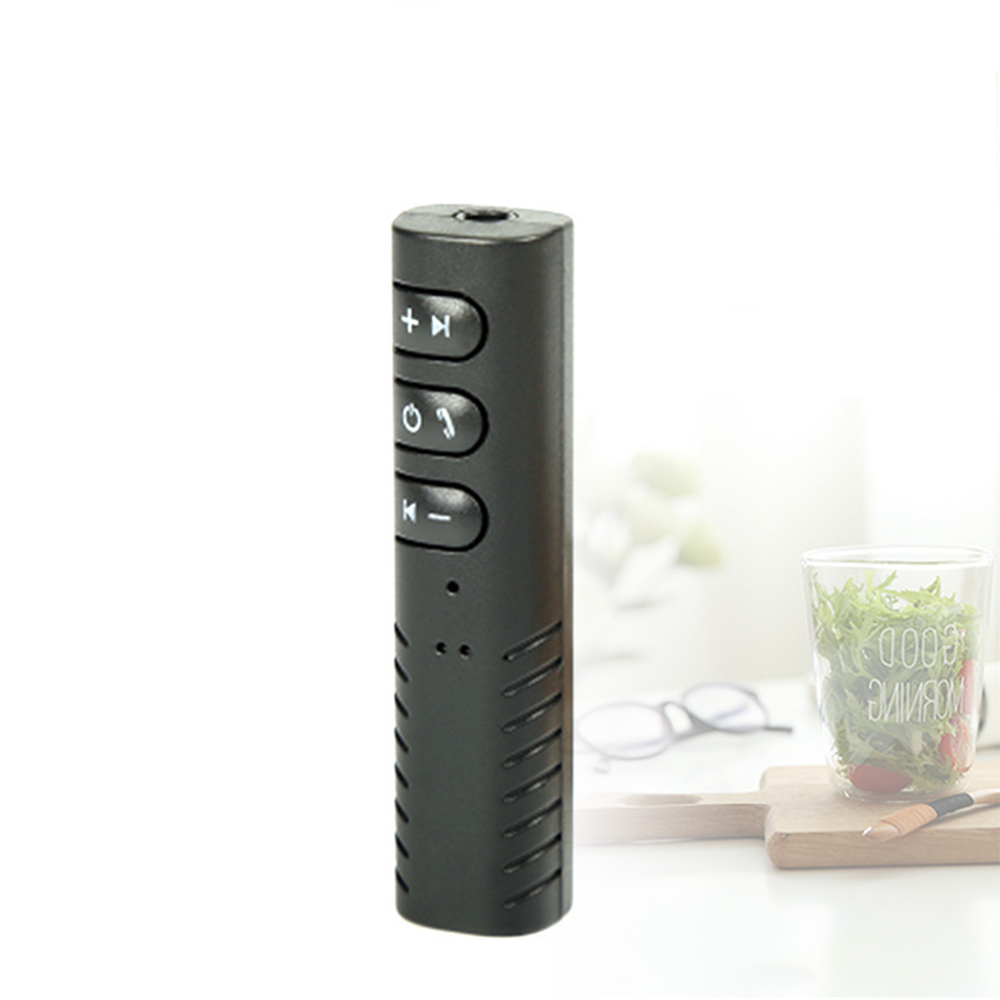 Ein schwarzes, rechteckiges Gerät mit Knöpfen, wahrscheinlich ein Bluetooth-Empfänger. Ein Glas mit Salat, Brille und ein Holzbrett im Hintergrund.