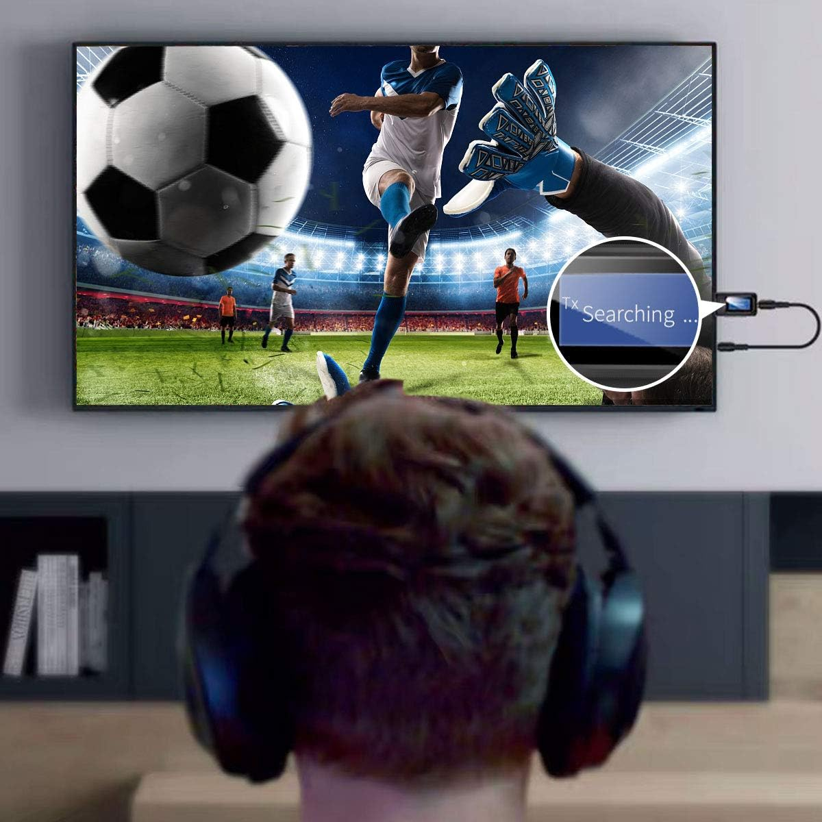 Eine Person mit Kopfhörern schaut ein Fußballspiel im Fernsehen. Der Fernseher zeigt einen Spieler, der den Ball tritt, mit 'Searching...' auf dem Bildschirm.
