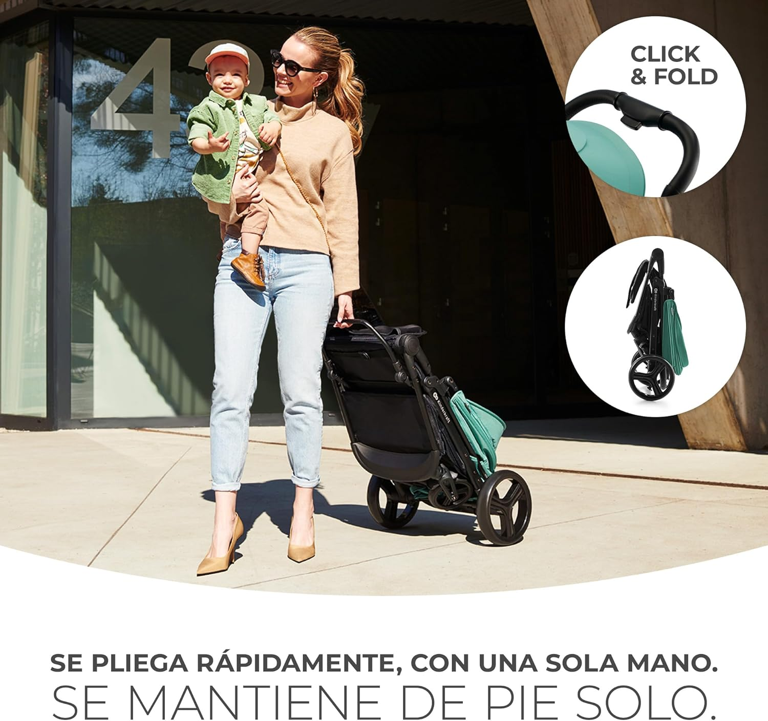 Una mujer sostiene a un bebé, de pie junto a un cochecito. El cochecito tiene un acento verde azulado, y la escena es al aire libre.