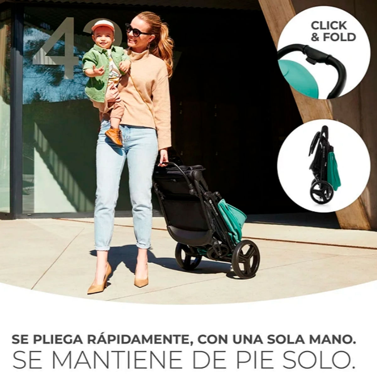 Una mujer sostiene a un bebé y un cochecito. El cochecito es negro y verde azulado. La mujer lleva gafas de sol y vaqueros.