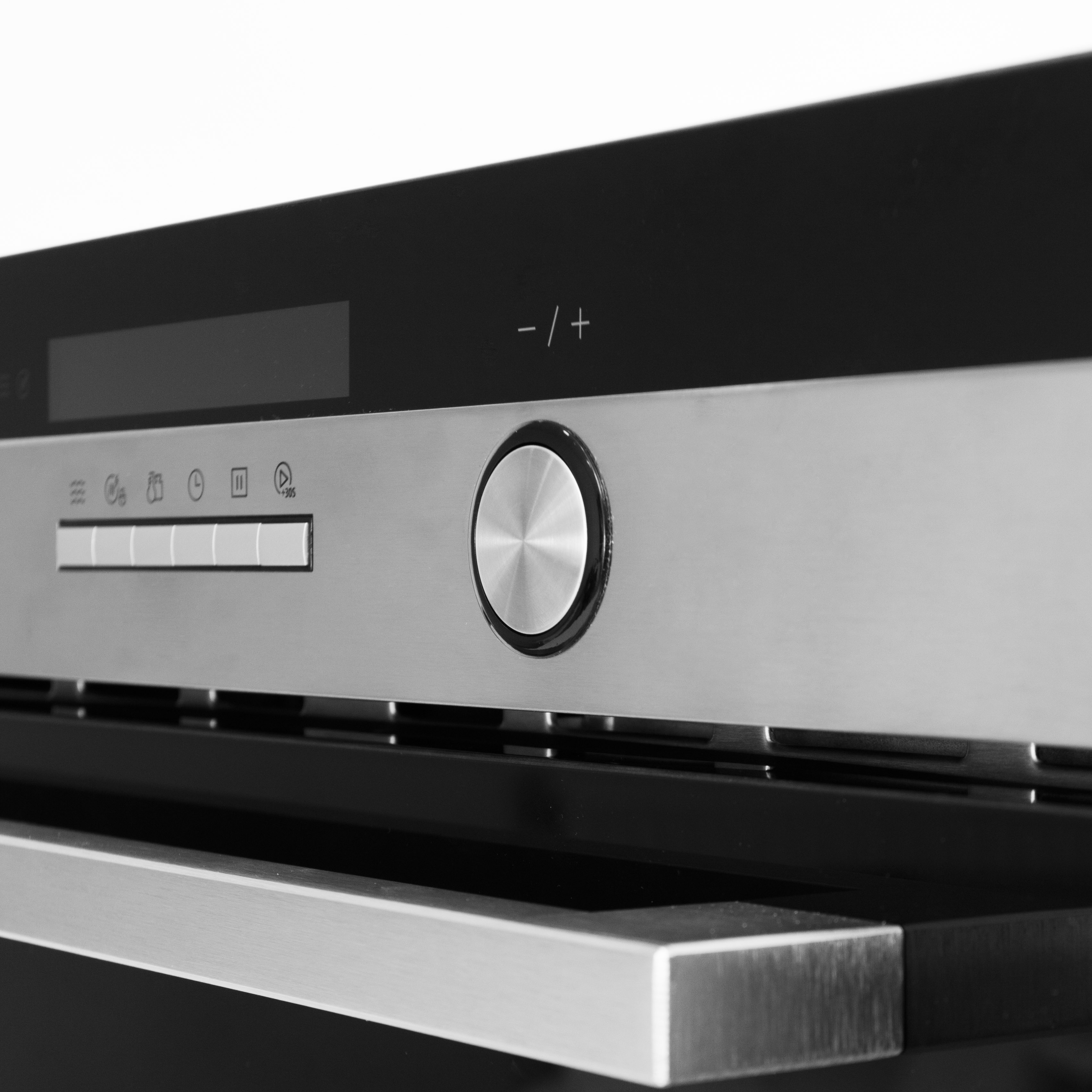 Close-up van een modern ovenbedieningspaneel. Het heeft een display, knoppen, een draaiknop en een handvat. Zilver en zwart.