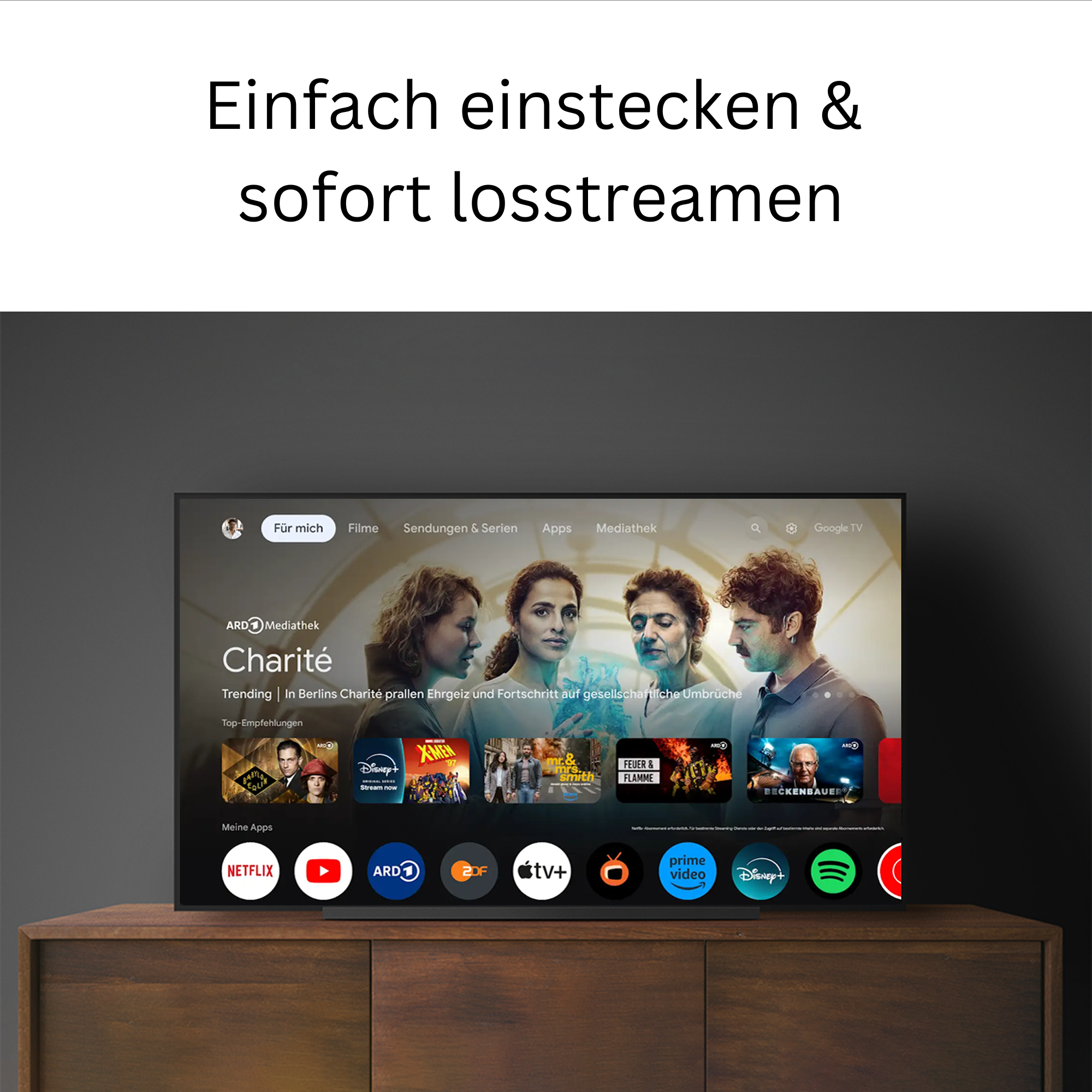 TV-Bildschirm auf einem Holzschrank. Der Bildschirm zeigt eine Streaming-Oberfläche mit App-Logos.