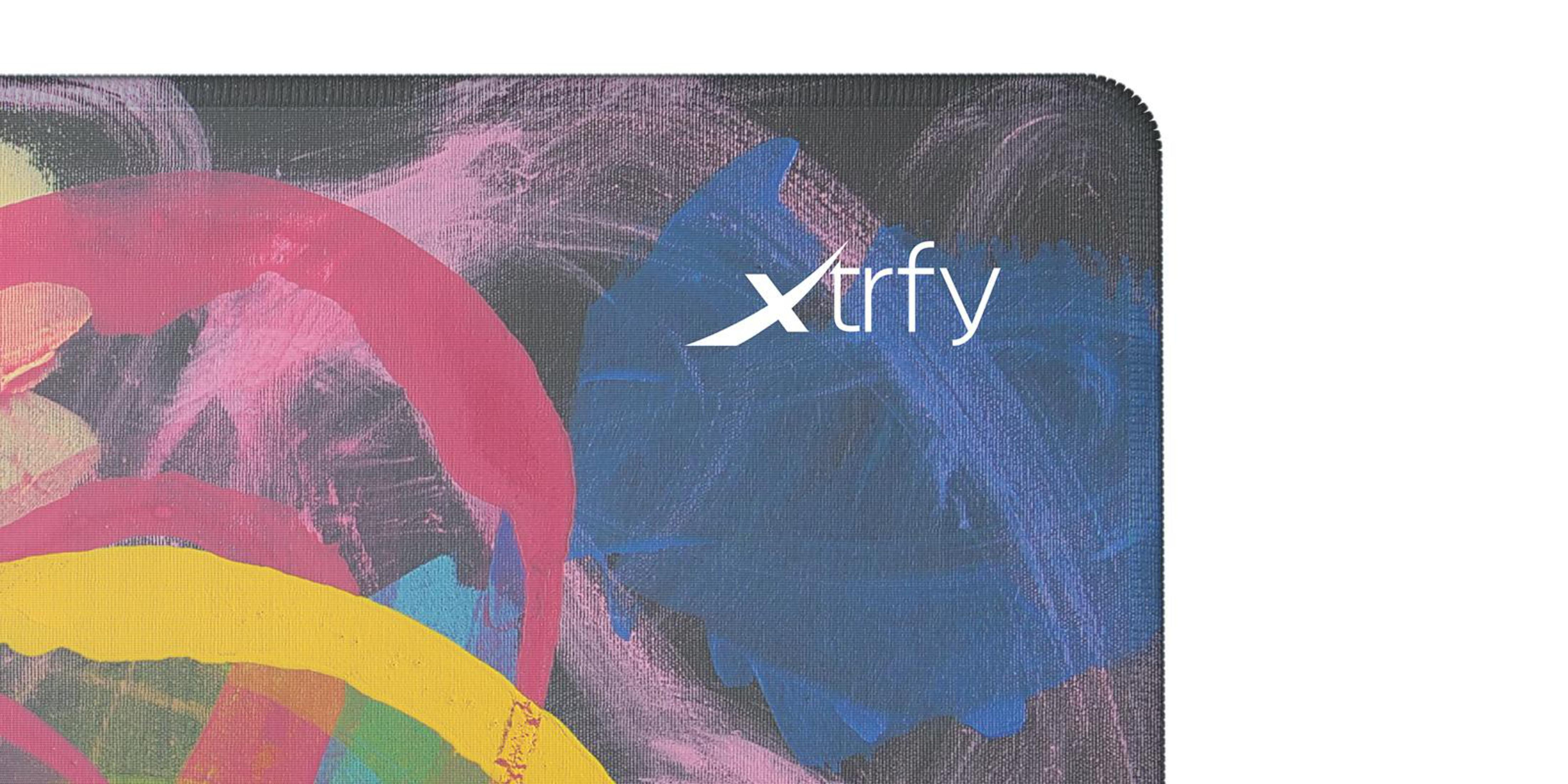 Tapis de souris avec design abstrait coloré. Coups de pinceau roses, jaunes et bleus avec logo blanc 'xtrfy' sur fond noir.