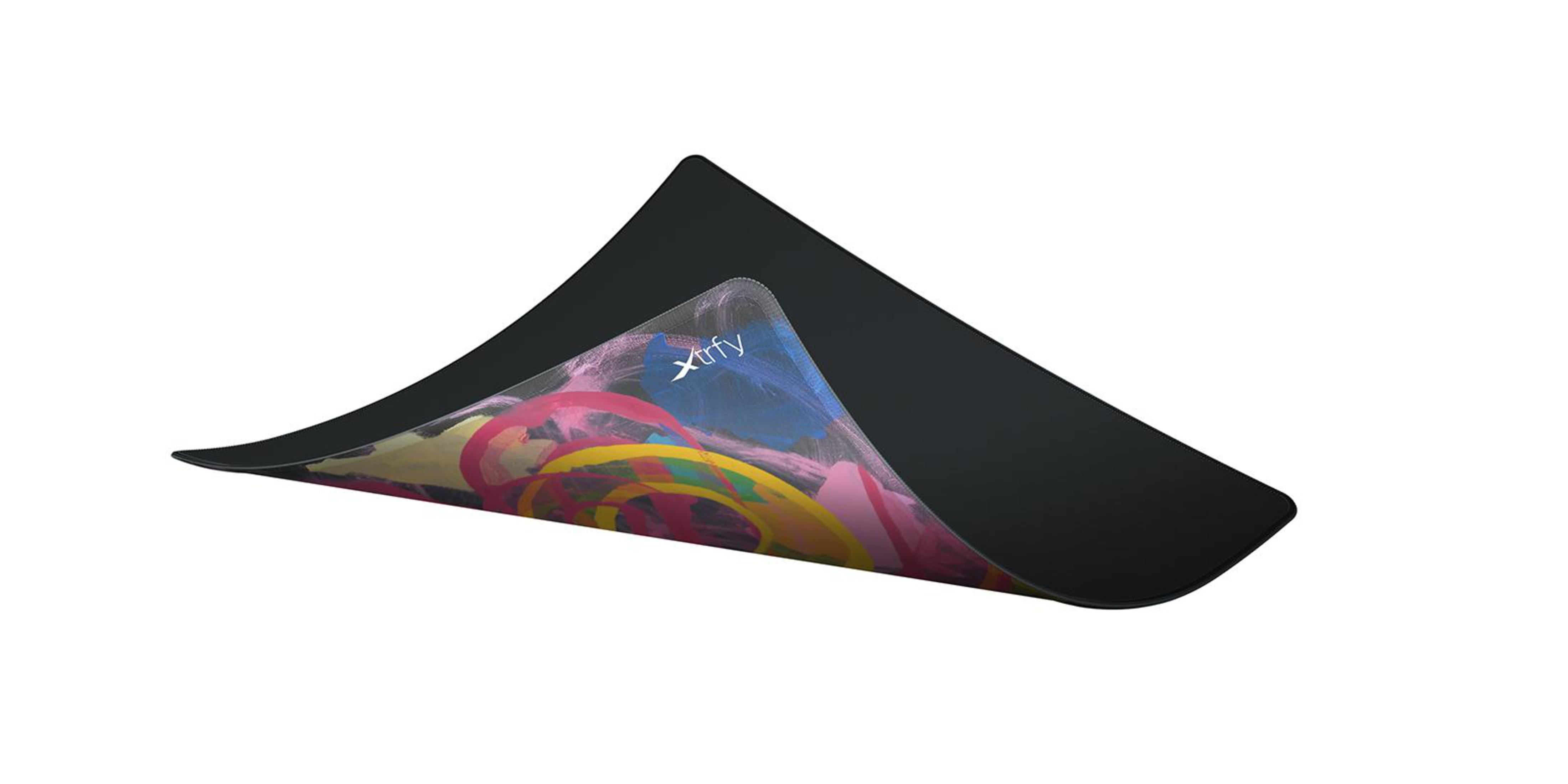 Tapis de souris Xtrfy noir, partiellement soulevé pour montrer le motif peint coloré en dessous. Fond blanc.