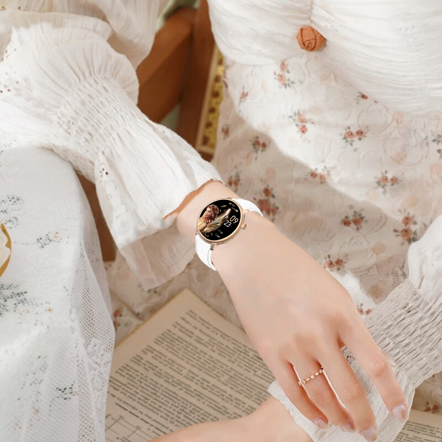 A woman wearing a white dress and a smartwatch. She's holding a book. A ring on her finger. Floral pattern on the dress.
