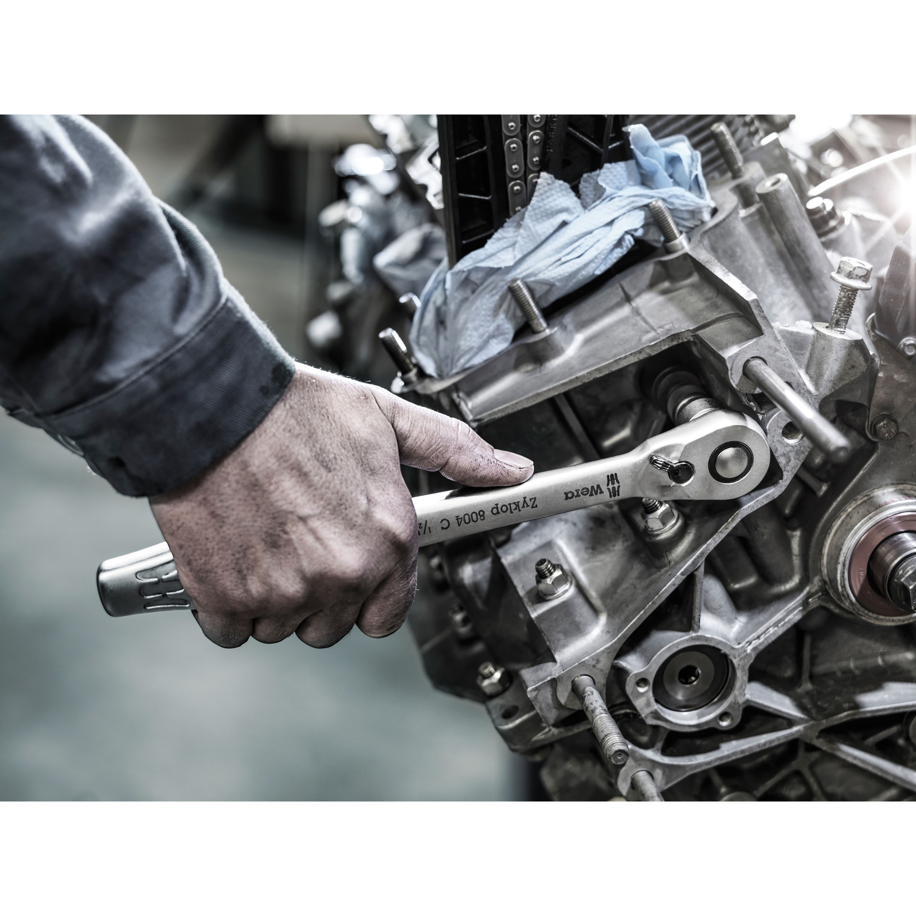 La mano di un meccanico usa una chiave a cricchetto Wera Zyklop 8004 C 1/2 su un motore. Il motore è argentato e c'è un panno blu.