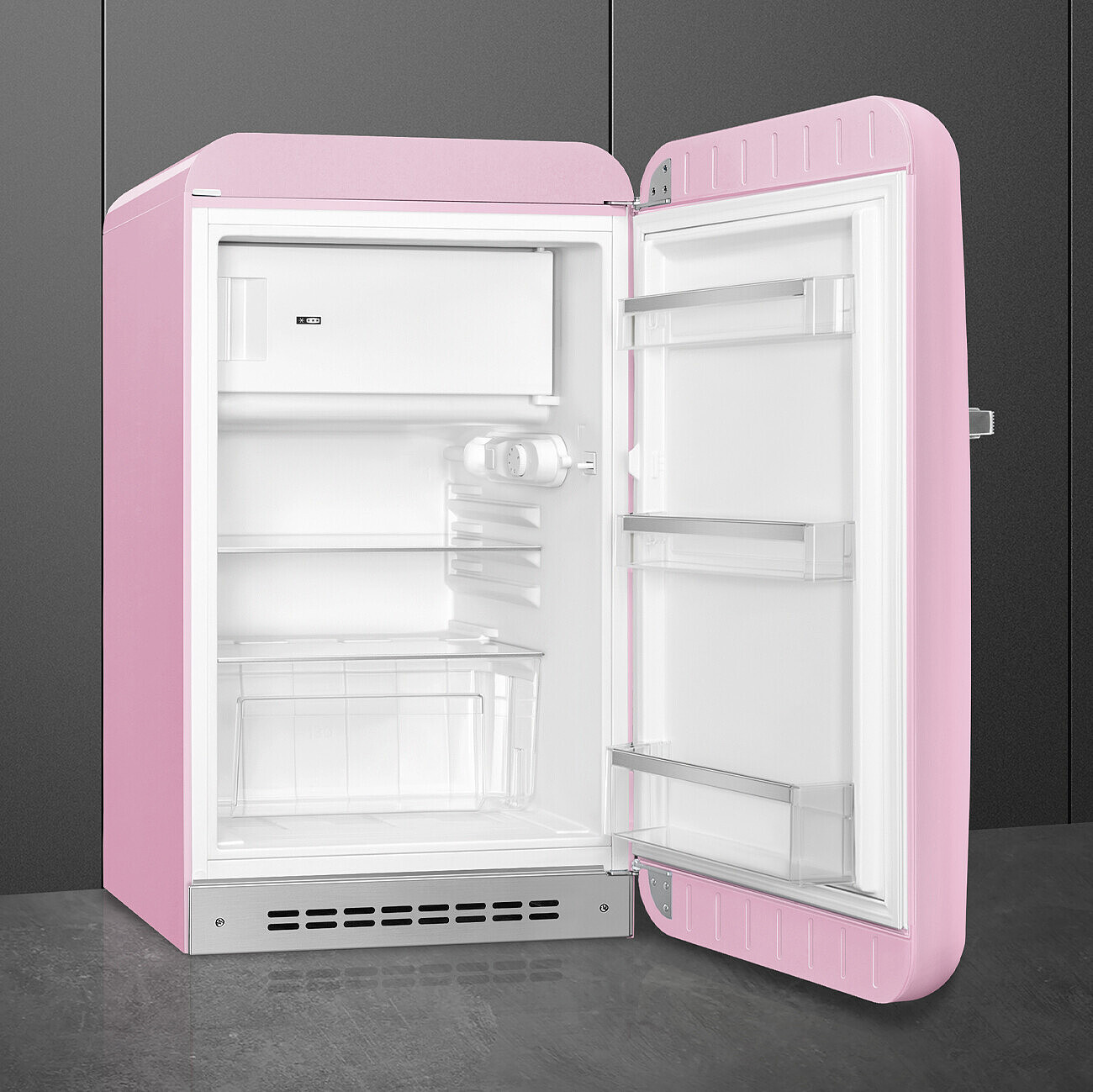 Un refrigerador retro rosa con la puerta abierta. El interior es blanco con estantes y un compartimento congelador. El fondo es gris.