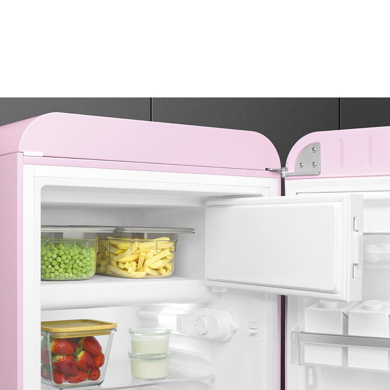 Refrigerador rosa con la puerta abierta, mostrando guisantes, papas fritas, fresas y productos lácteos. La puerta está abierta.