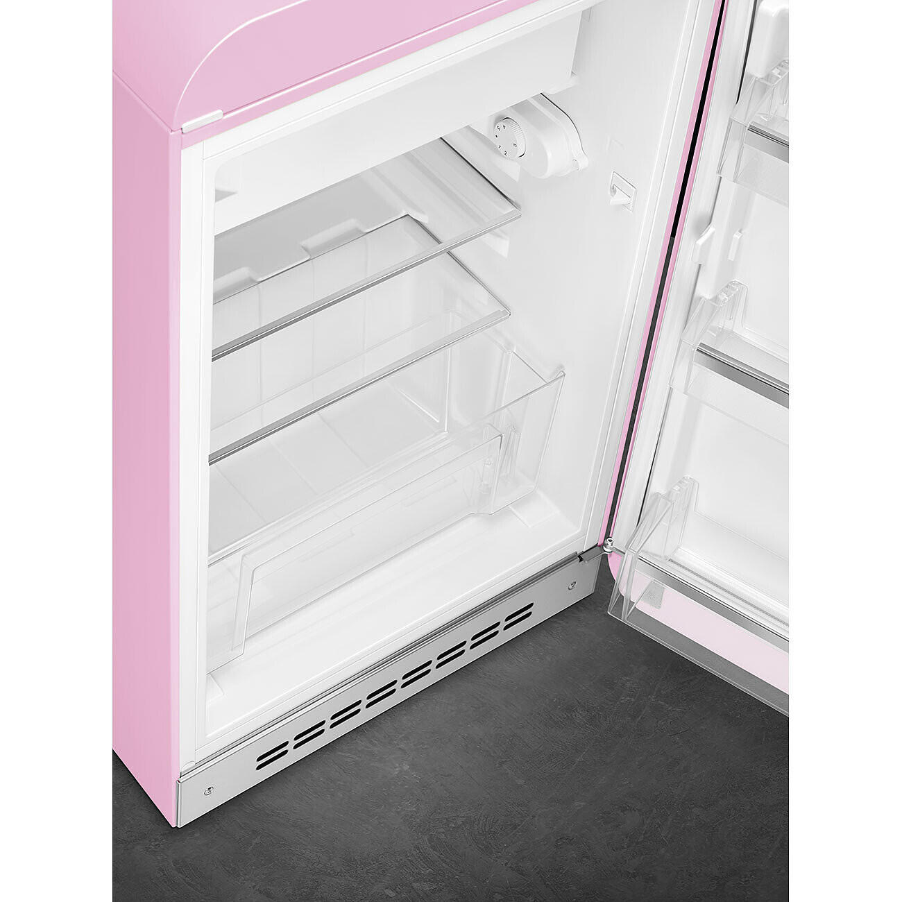Refrigerador retro rosa con la puerta abierta. En el interior, se ven estantes y cajones transparentes. El suelo es gris oscuro.