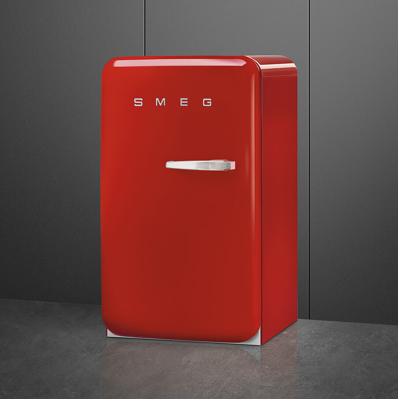 Un frigorifero SMEG rosso è appoggiato a una parete grigia. Il frigorifero ha una maniglia argentata e il logo SMEG.