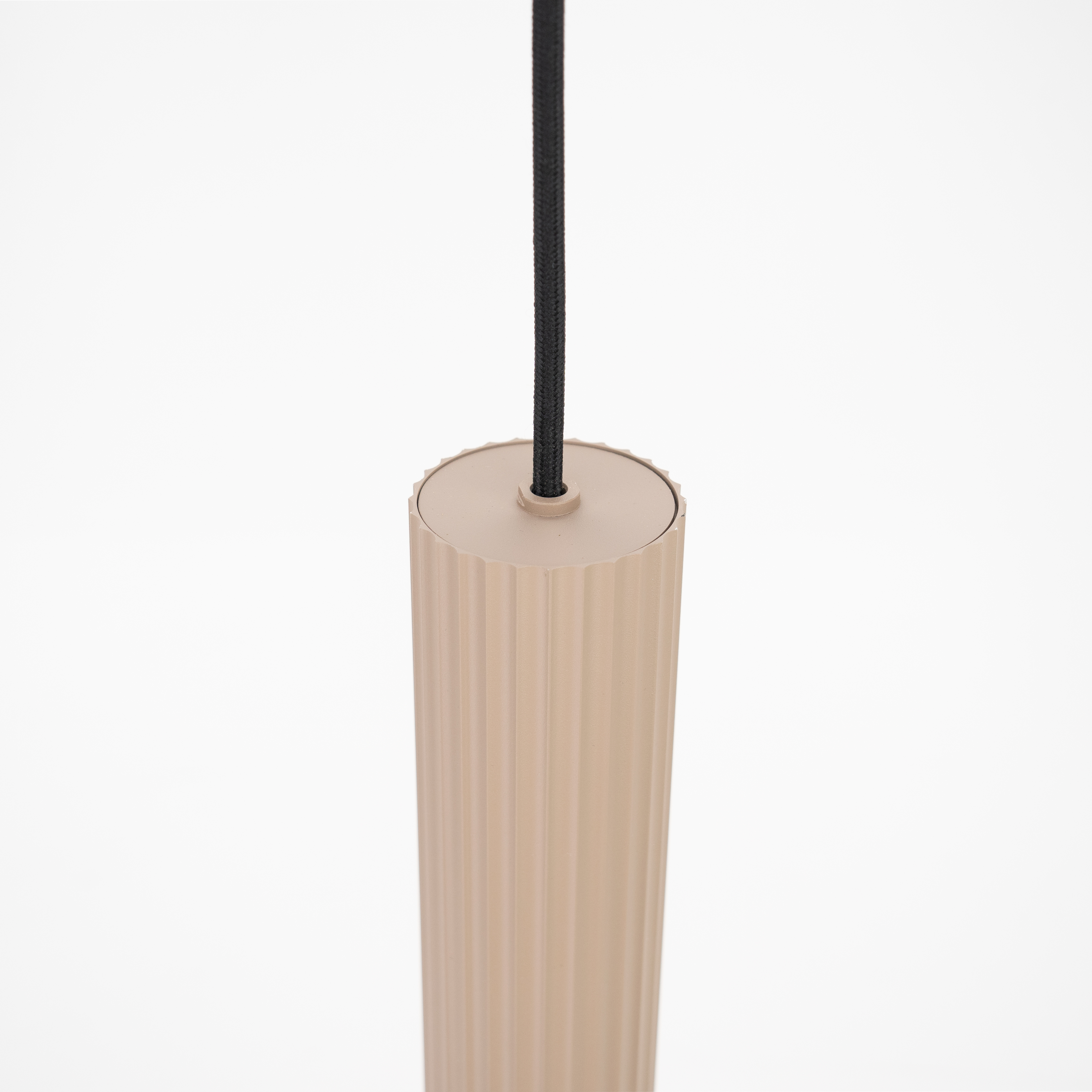 Una lámpara cilíndrica beige y acanalada cuelga de un cable negro sobre un fondo blanco.