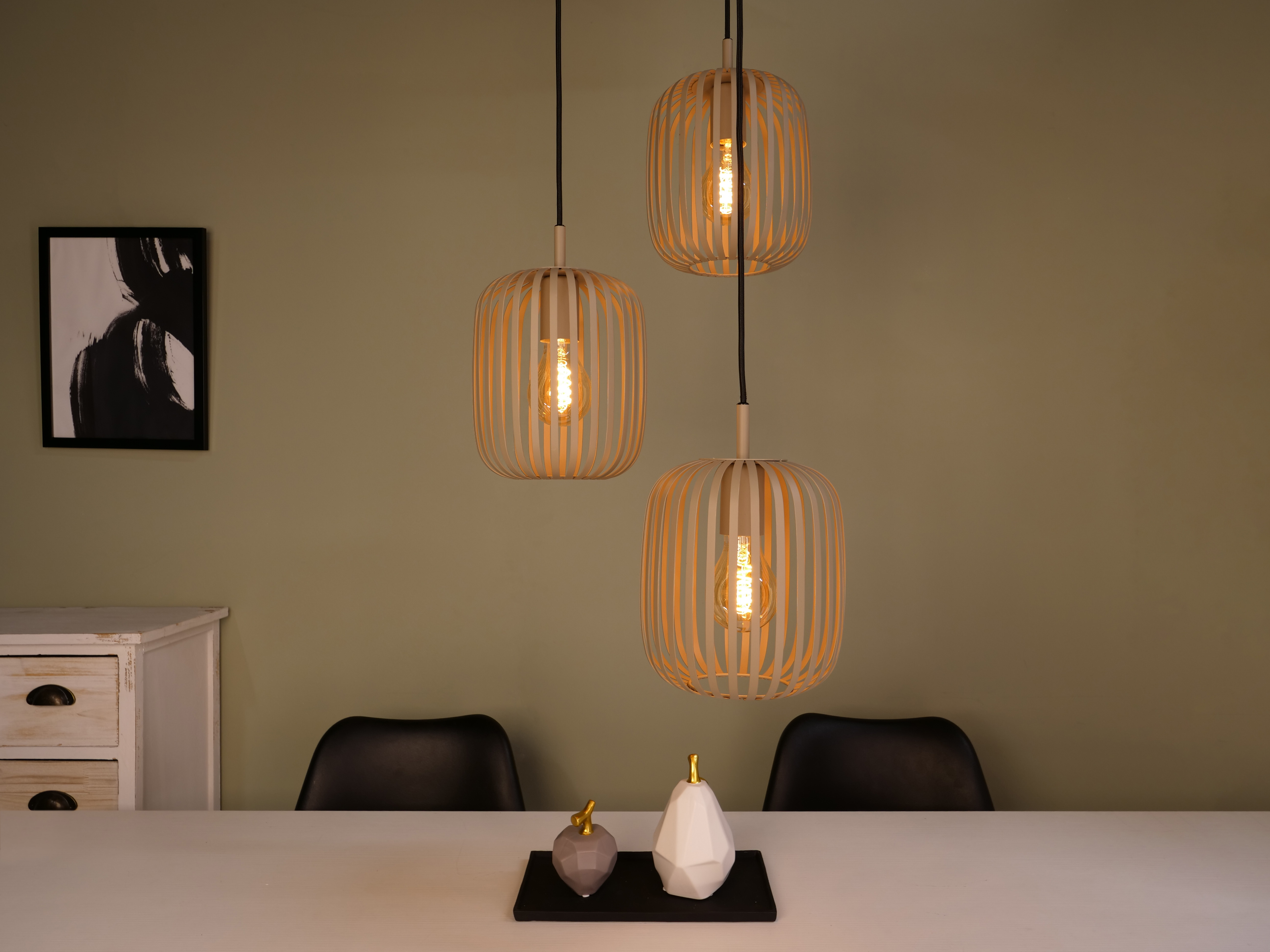 Drie hanglampen met warme lampen. Een tafel met decoratie, stoelen en een schilderij in de kamer.