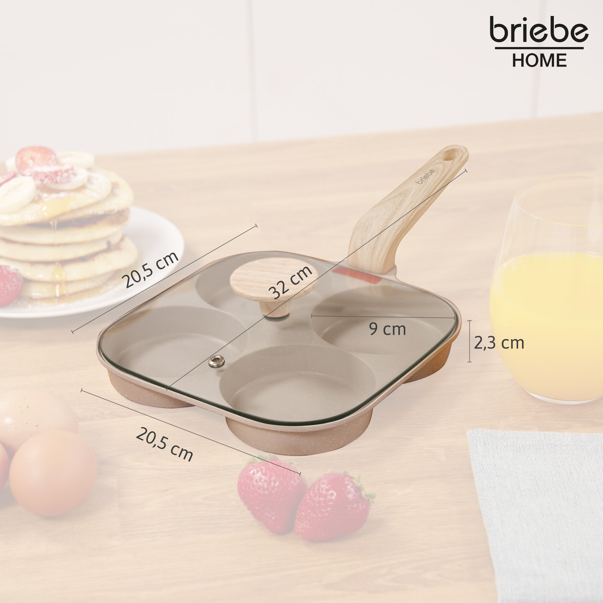 Una sartén con cuatro moldes redondos, tapa de cristal y mango de madera. Medidas mostradas. Panqueques, fresas y jugo en el fondo.