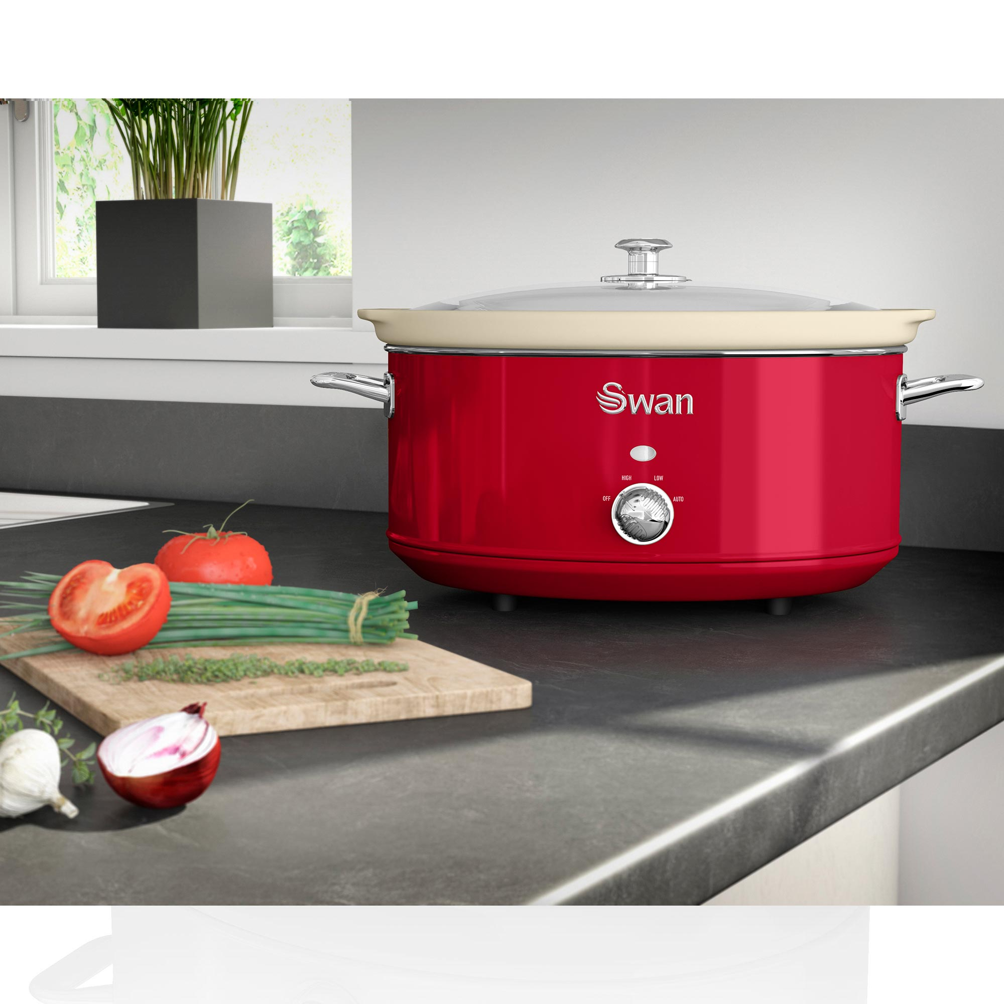 Roter Slow Cooker mit Deckel, Gemüse und Kräutern auf einem Schneidebrett und Pflanze in einem Topf, alles auf einer Arbeitsplatte.