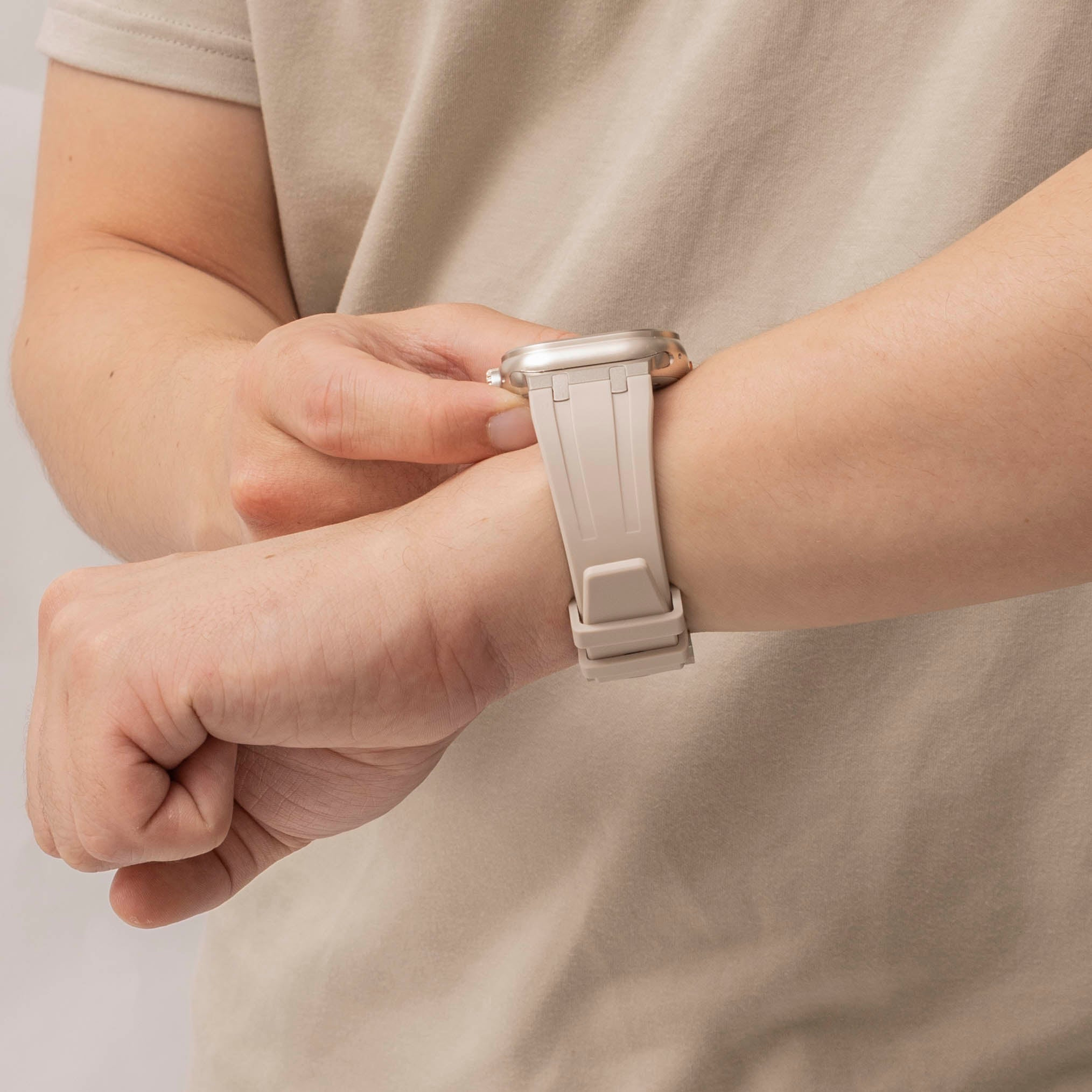 Eine Person mit einer beigen Uhr schaut auf die Uhrzeit. Die Uhr hat ein beiges Armband und ein silbernes Gehäuse. Die Person trägt ein beiges Hemd.