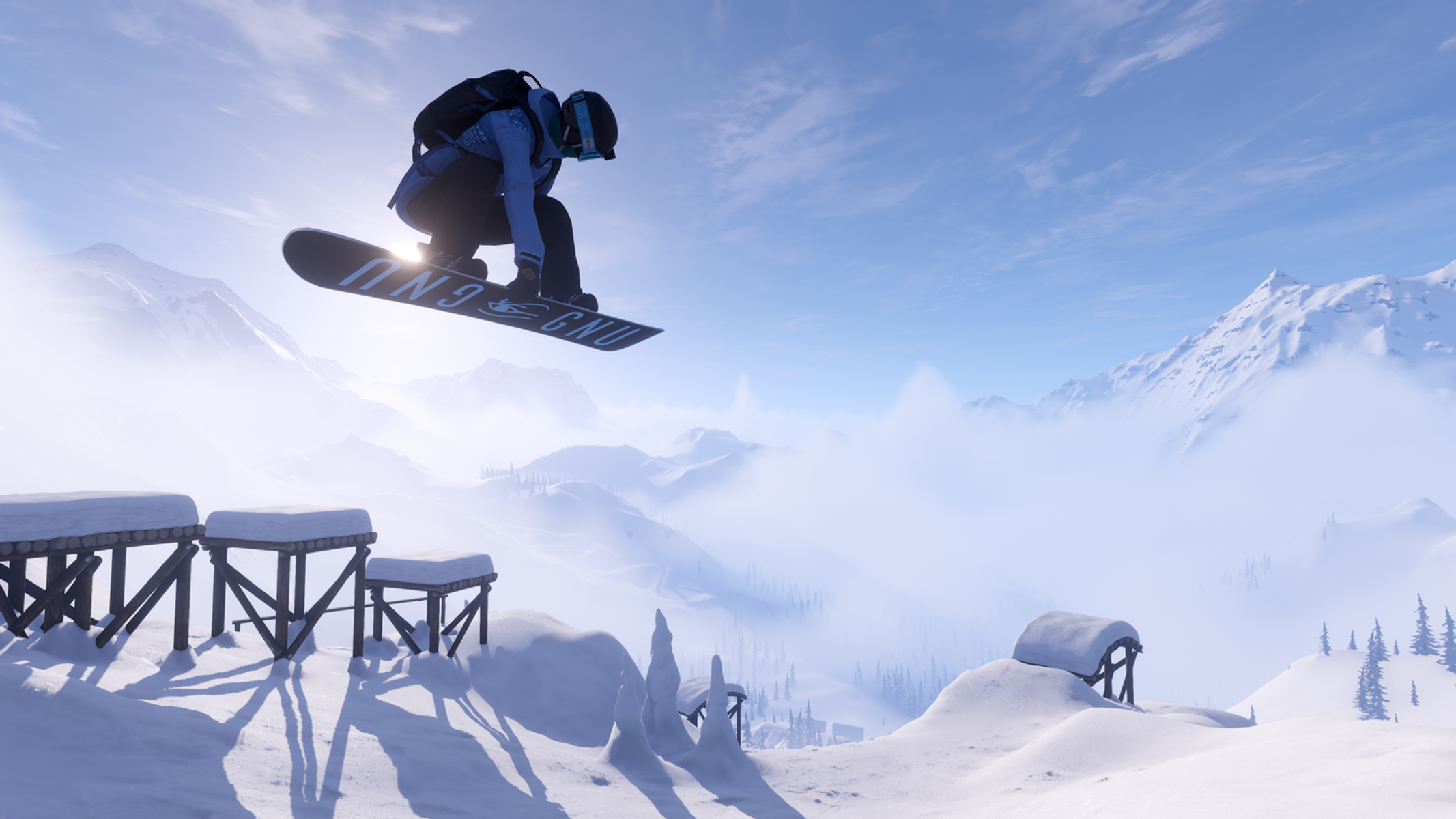 Snowboardzista skacze nad pokrytymi śniegiem drewnianymi konstrukcjami, w tle zaśnieżony łańcuch górski.
