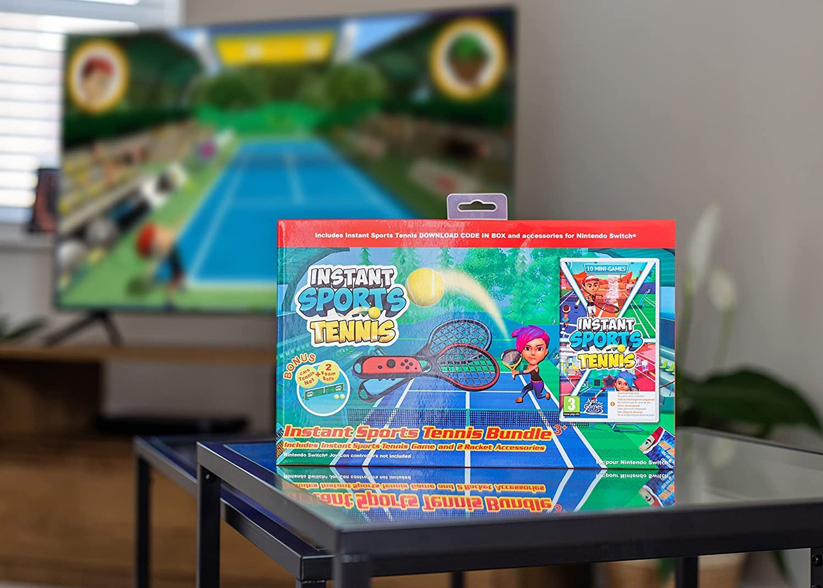 Pudełko z grą Instant Sports Tennis Bundle leży na stole. Rozmyty telewizor w tle pokazuje mecz tenisa.