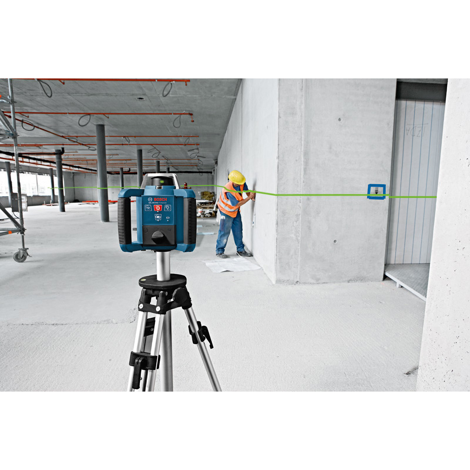 Bir inşaat işçisi lazer seviyesi kullanıyor. Bir tripod üzerindeki mavi lazer seviyesi, beton bir duvara yeşil bir çizgi yansıtıyor.