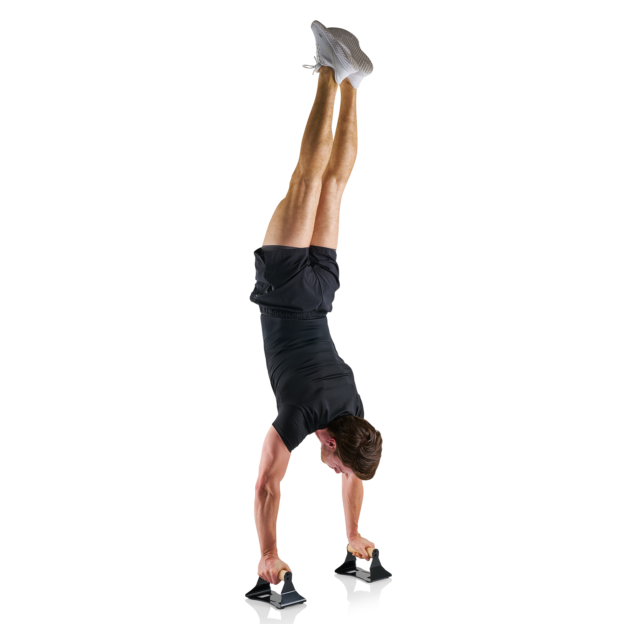 Ein Mann in schwarzer Sportkleidung macht einen Handstand mit Liegestützgriffen. Beine hoch, Füße zeigen. Weißer Hintergrund.