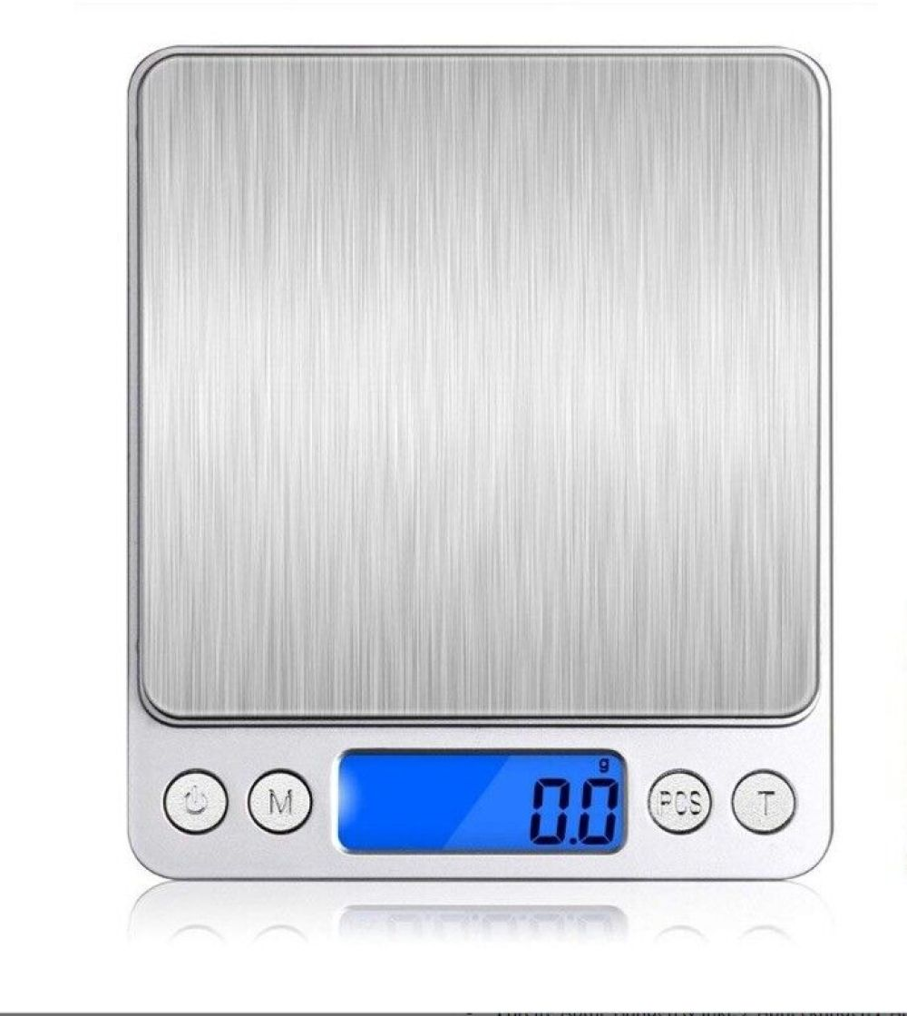 Eine digitale Küchenwaage. Sie hat eine Edelstahloberfläche und ein blaues Display mit der Anzeige '0,0'. Es gibt Tasten mit den Bezeichnungen 'M', 'PCS' und 'T'.