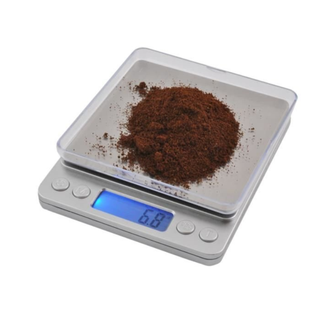 Eine Digitalwaage mit braunem Kaffeemehl. Der Bildschirm zeigt '6.8'. Die Waage ist silberfarben mit einer durchsichtigen Kunststoffschale.