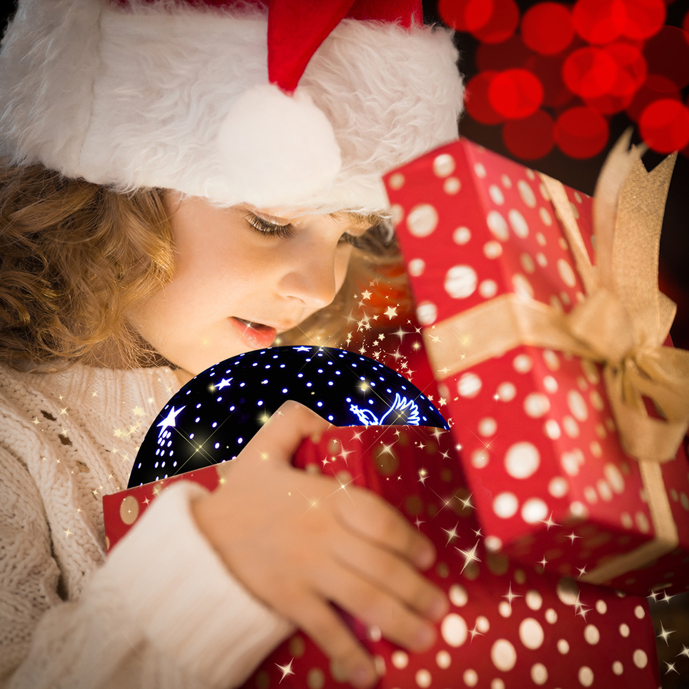 Ein Kind mit Weihnachtsmütze öffnet eine Geschenkbox. Innen ein leuchtendes Sternennachtszenario. Eine weitere Geschenkbox ist vorhanden.