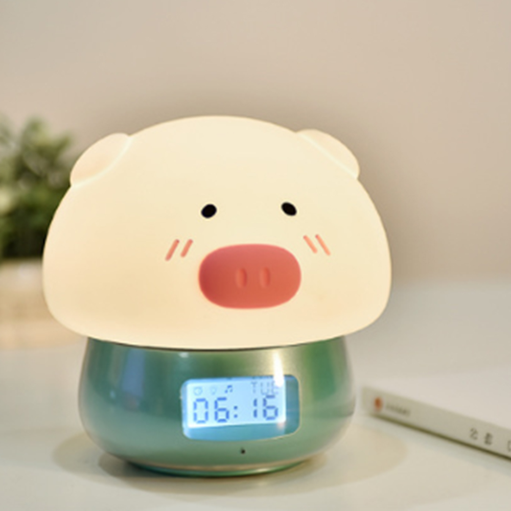 Ein schweineförmiger Wecker zeigt 06:16 Uhr an. Die Uhr ist hellgrün mit einem Schweinegesicht oben und steht auf einem Tisch.