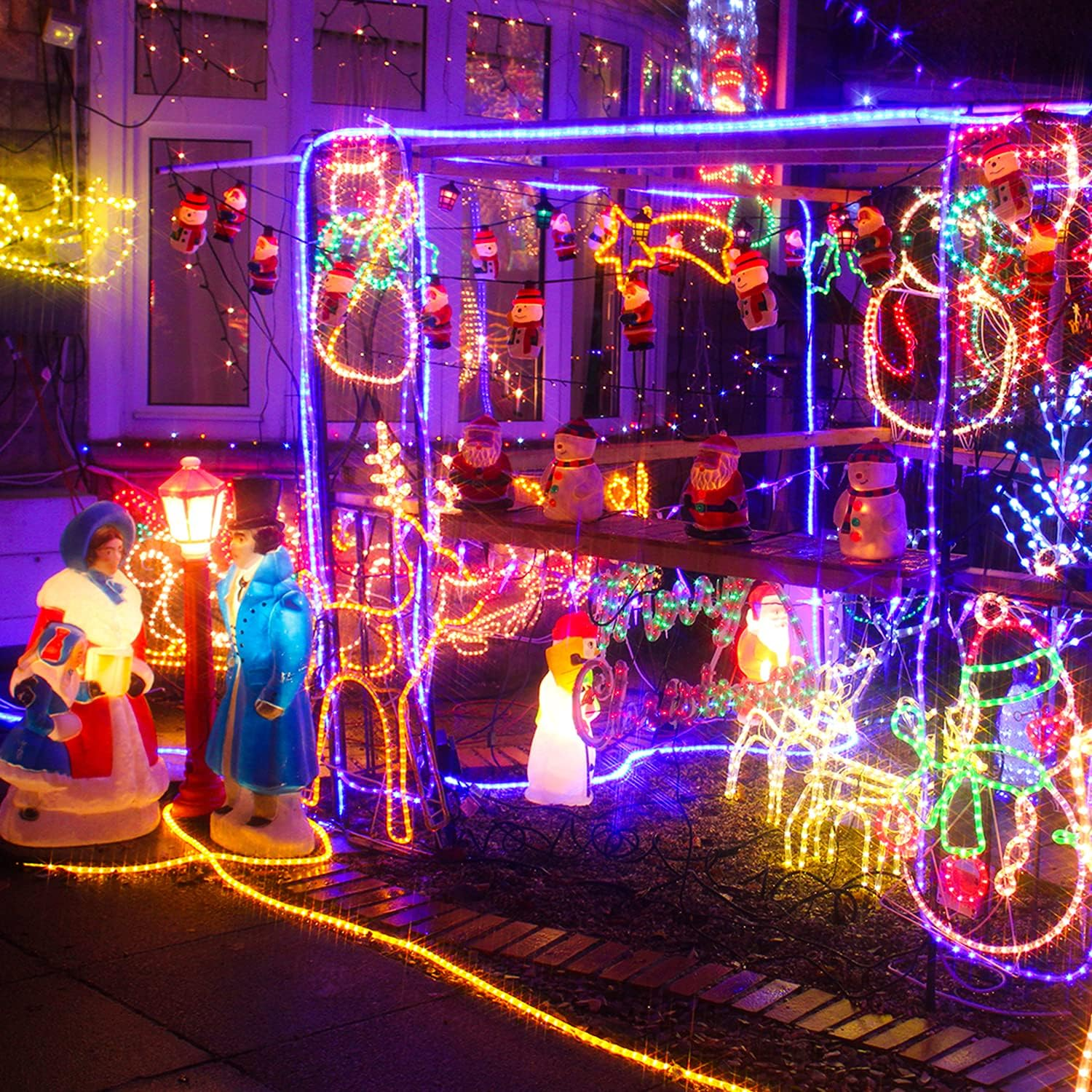 Ein Haus ist mit Weihnachtsbeleuchtung geschmückt. Weihnachtsmann, Schneemann und Rentierfiguren sind beleuchtet. Bunte Lichterketten schmücken Haus und Garten.