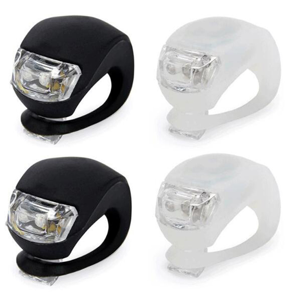 Vier kleine Fahrradlichter. Zwei sind schwarz, zwei weiß. Jedes hat eine klare Linse und eine gummierte Schlaufe.