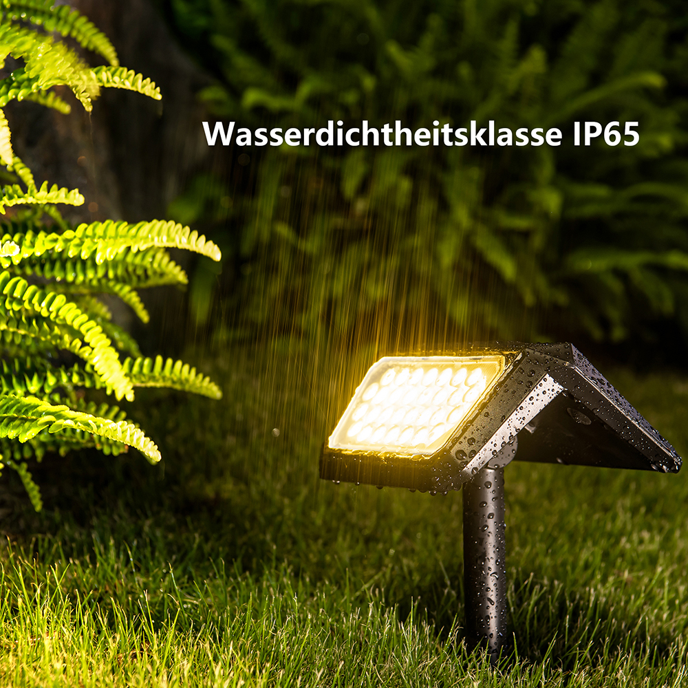 Eine solarbetriebene Leuchte beleuchtet einen Rasen. Regen fällt, und üppige grüne Pflanzen umgeben das Licht. Text: Wasserdichtheitsklasse IP65.