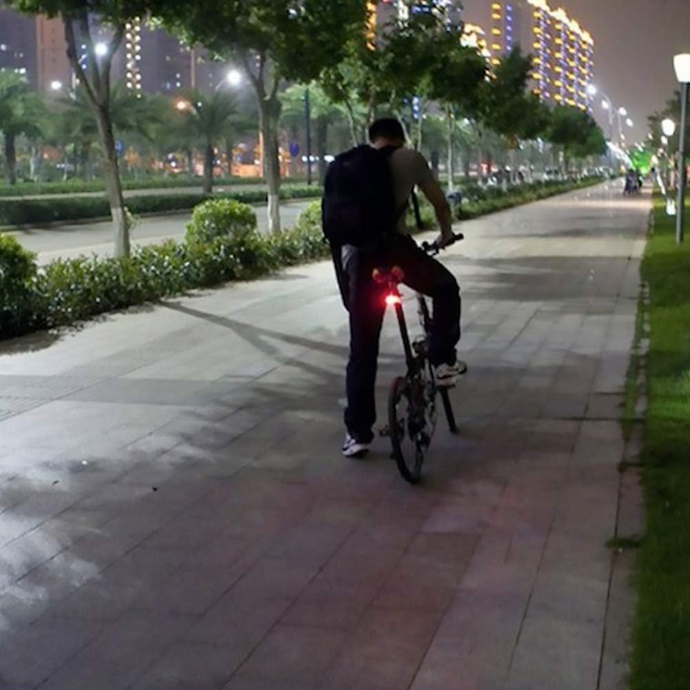 Eine Person fährt nachts Fahrrad. Das Fahrrad hat ein rotes Licht. Im Hintergrund sind Gebäude und Straßenlaternen.