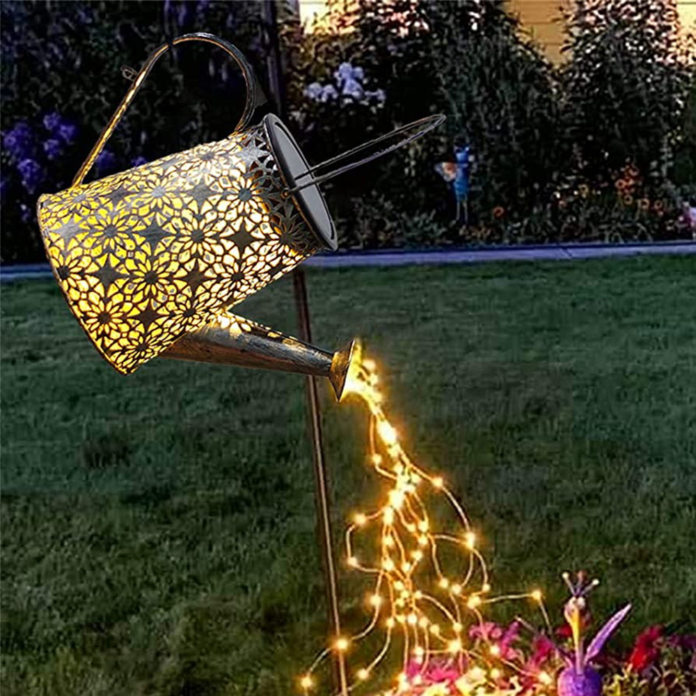 Eine dekorative Gießkanne mit floralem Design. Sie scheint einen Wasserfall aus Lichtern auf ein Blumenbeet zu gießen.
