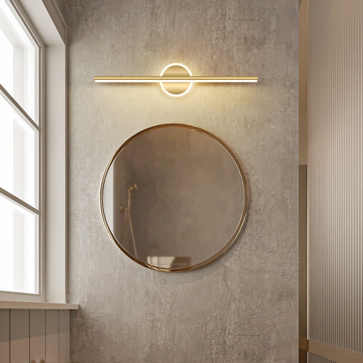 Badezimmer mit rundem Spiegel, goldfarbener Leuchte und Fenster. Die Wand ist grau strukturiert.