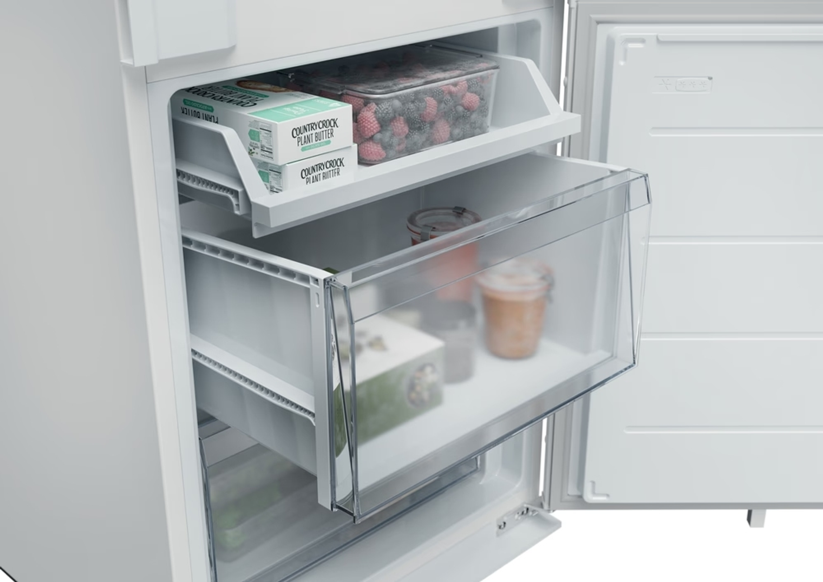 Un frigorifero è aperto. All'interno ci sono cassetti con alimenti come bacche, burro e barattoli. Il frigorifero è bianco.