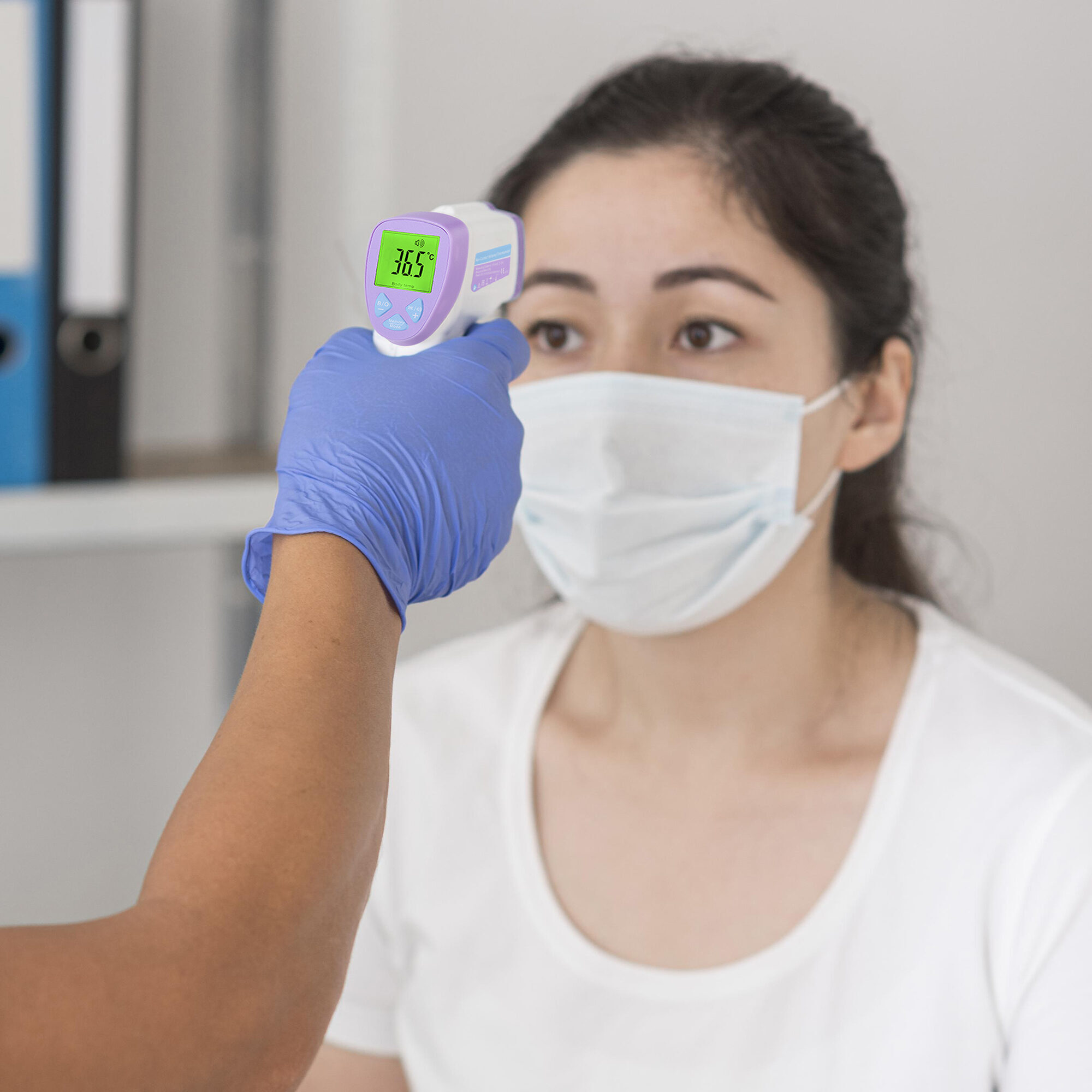 Una persona controla la temperatura de otra con un termómetro infrarrojo. La persona lleva mascarilla y la otra un guante.