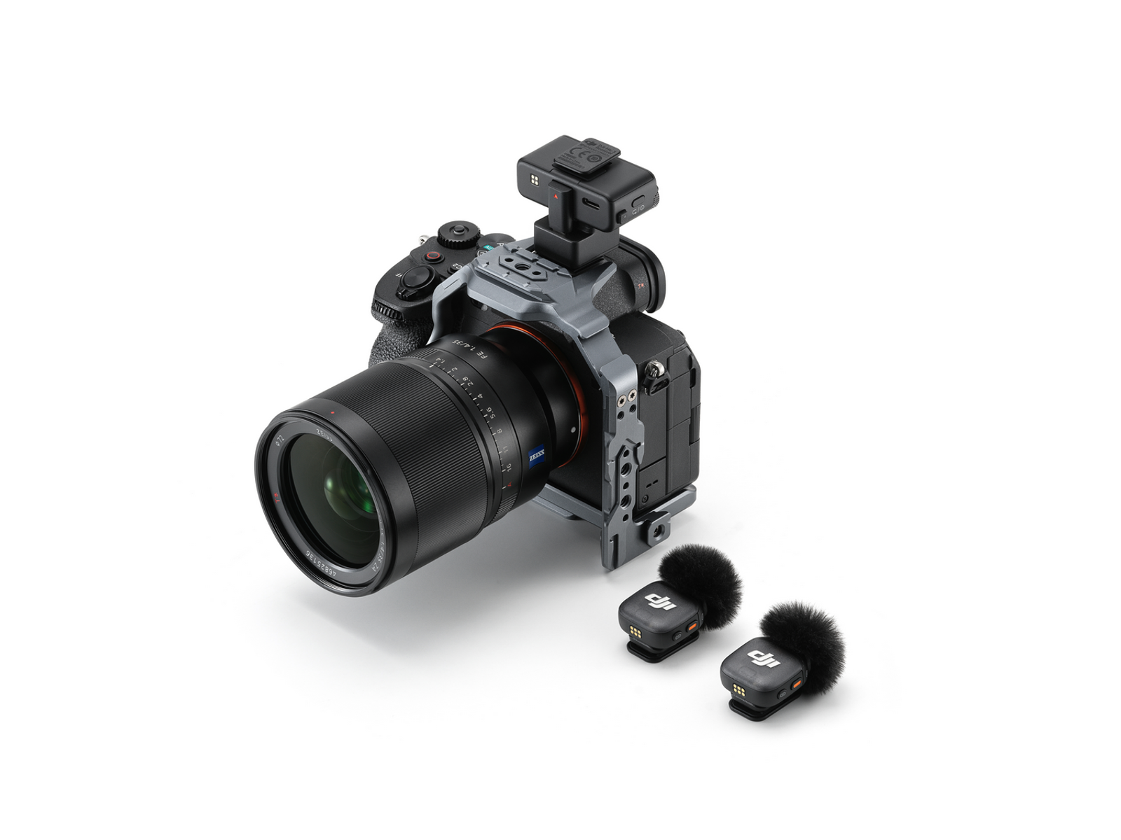 Beyaz zeminde lens ve aksesuarlarla bir kamera. Önünde iki mikrofon var. Siyah ve gümüş renkler hakim.