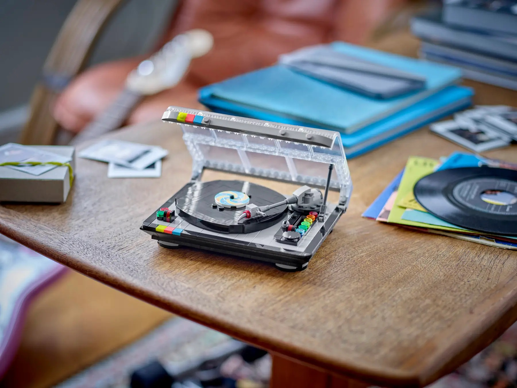 Un giradischi Lego è su un tavolo di legno. Dischi, una chitarra e libri sono sullo sfondo.