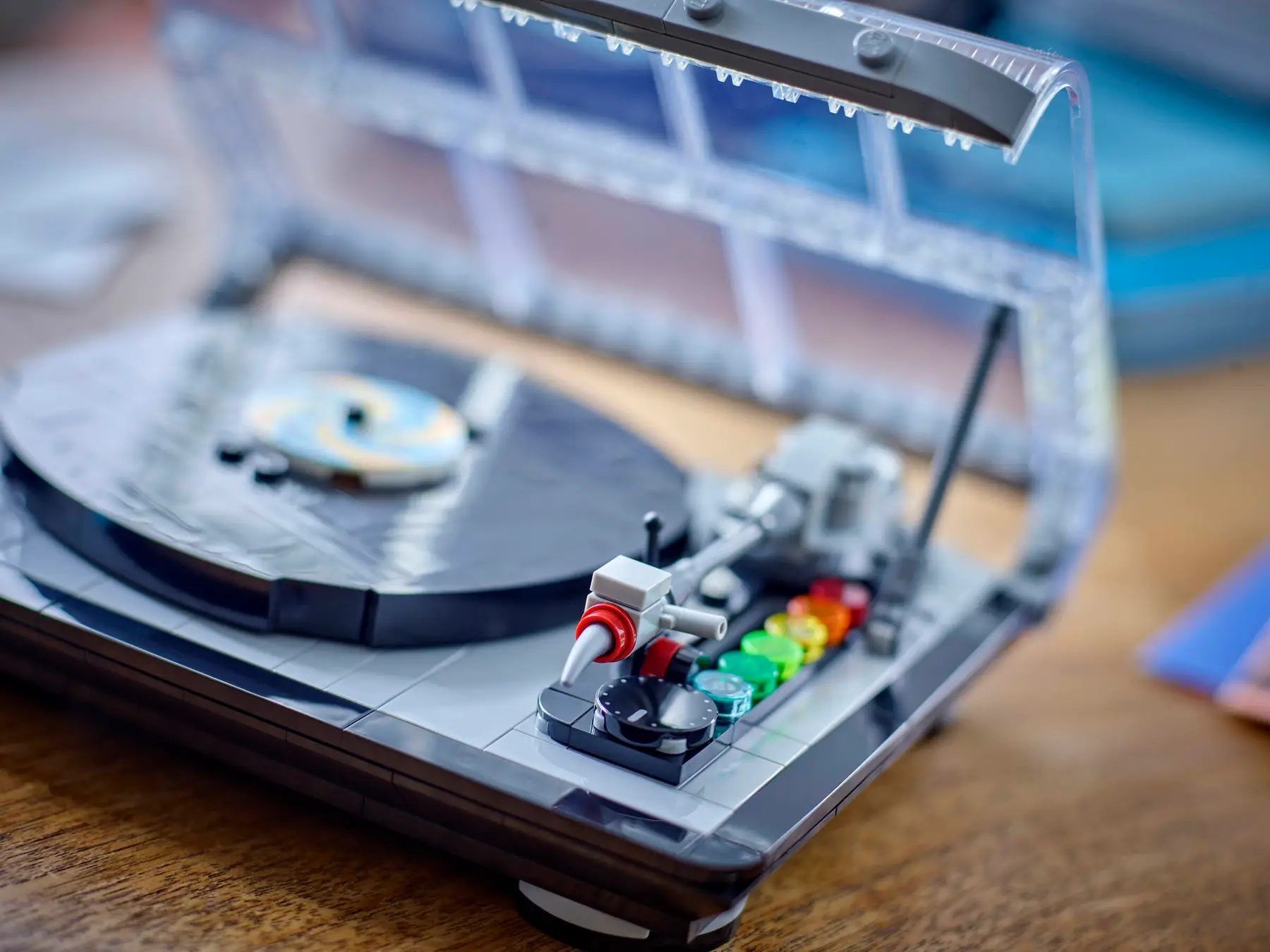 Un giradischi Lego con coperchio trasparente. Il giradischi è grigio e nero, con pulsanti colorati e un disco.