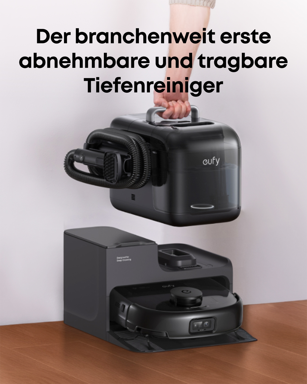 Czarny odkurzacz jest trzymany nad stacją ładującą. Górna część jest odłączana. Widoczna jest marka 'eufy'.