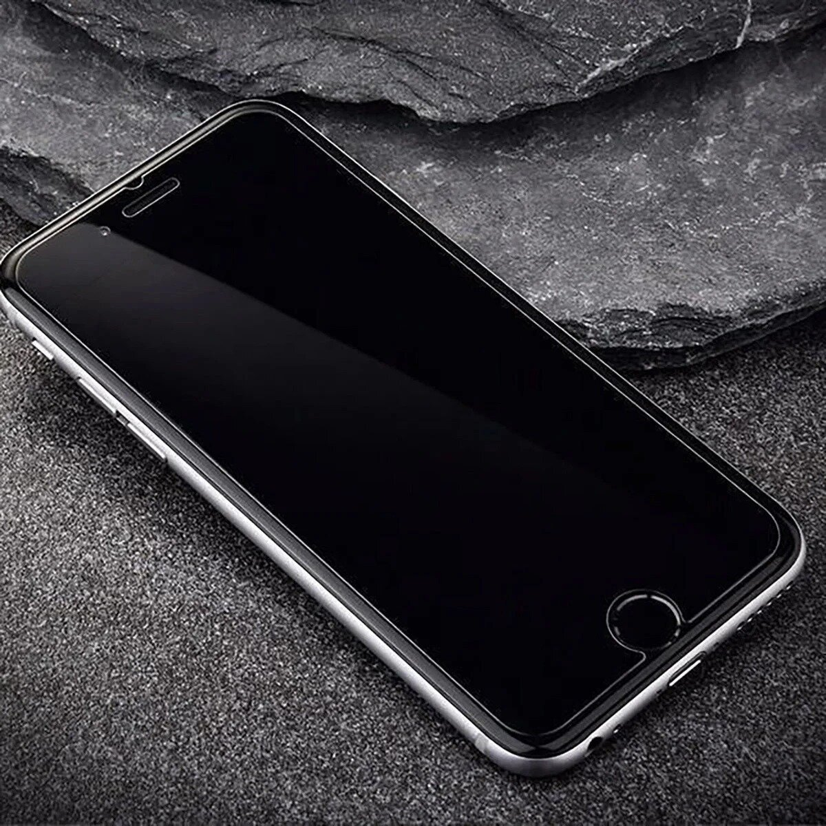 Een smartphone met een zwarte schermbeschermer ligt op een getextureerd, donkergrijs stenen oppervlak. De telefoon heeft een zilveren frame.