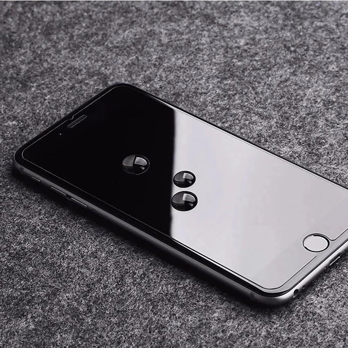 Een zwarte smartphone met waterdruppels op het scherm, geplaatst op een grijze, getextureerde ondergrond. De telefoon heeft een ronde knop.
